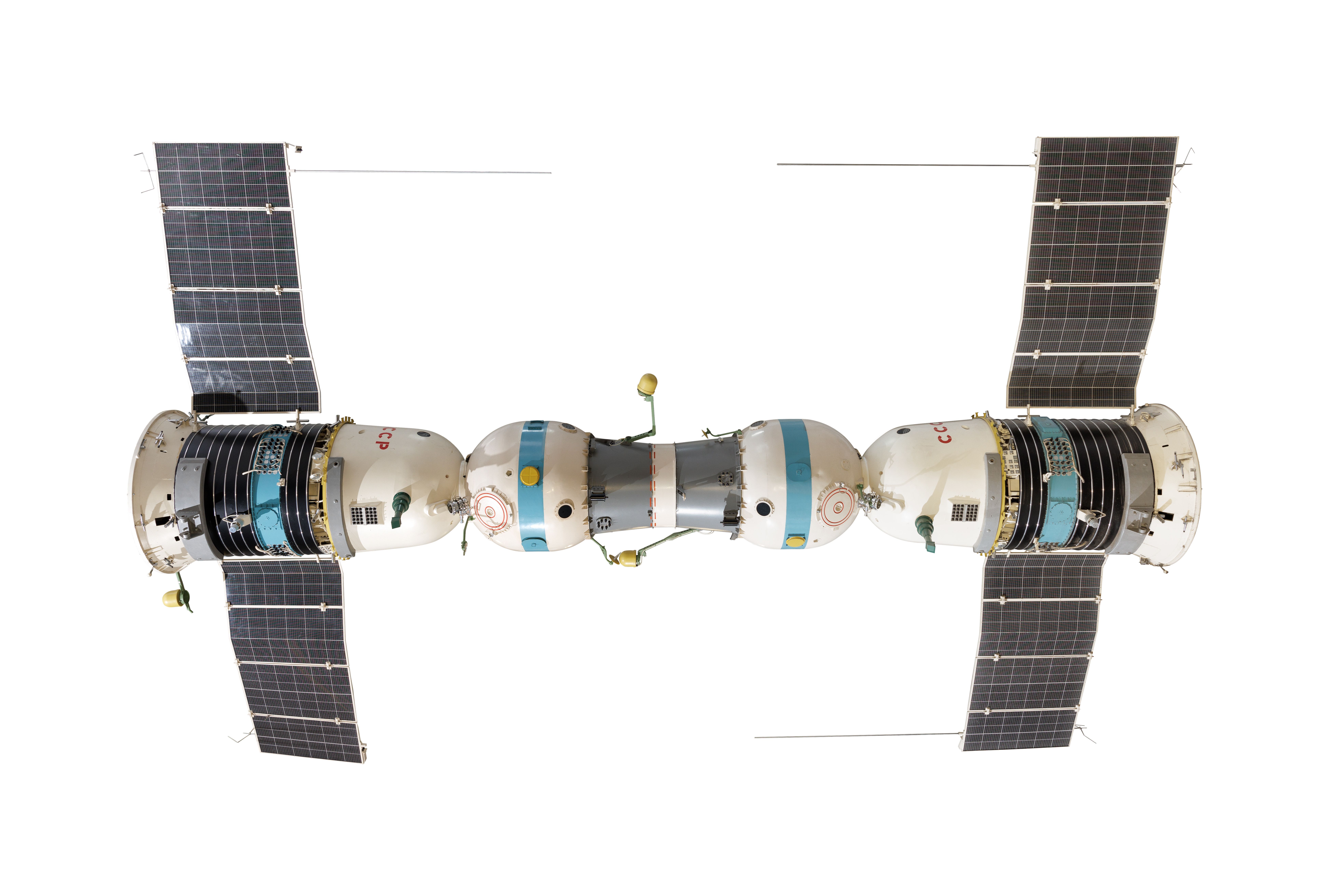 Photograph of a 1:3 scale model of the Soyuz-4 and Soyuz-5 crewed spacecraft link-up. Each Soyuz spacecraft consists of a spherical 'orbital module'at the front, a bell-shaped re-entry module in the middle of the craft, with a cylindrical service module at the rear. Long solar panels extend from either side of the service module. The two craft are joined nose-to-nose by a short, cylindrical docking tunnel, painted grey. Two sections of metal antenna are detached from the model.