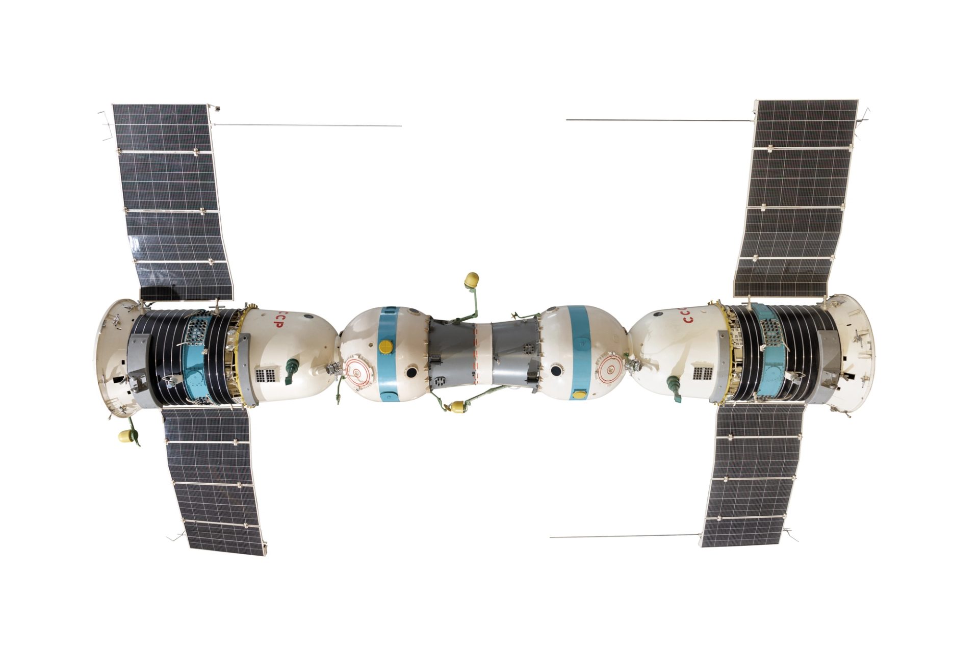 Photograph of a 1:3 scale model of the Soyuz-4 and Soyuz-5 crewed spacecraft link-up. Each Soyuz spacecraft consists of a spherical 'orbital module'at the front, a bell-shaped re-entry module in the middle of the craft, with a cylindrical service module at the rear. Long solar panels extend from either side of the service module. The two craft are joined nose-to-nose by a short, cylindrical docking tunnel, painted grey. Two sections of metal antenna are detached from the model.