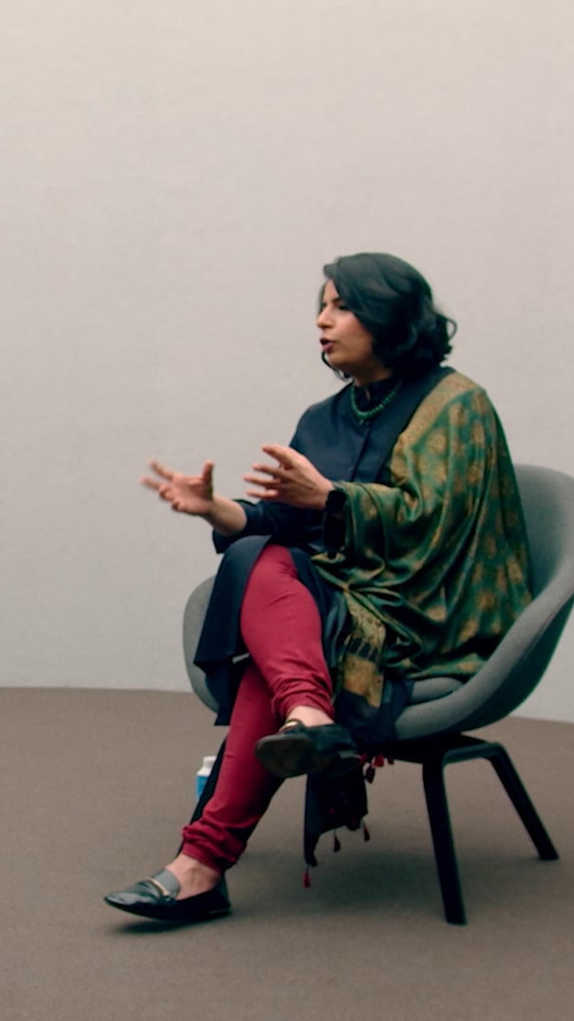 Two figures sitting on chairs in conversation.