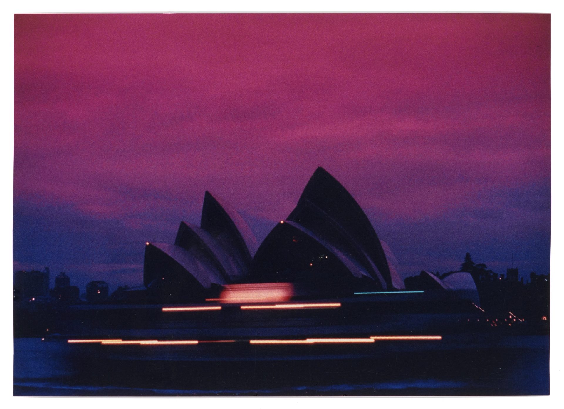 Glossy type C colour photograph of the Sydney Opera House taken with slow exposure at sunset from Sydney Harbour looking south-west. There is a moving ferry in the foreground which appears as lines of light.
