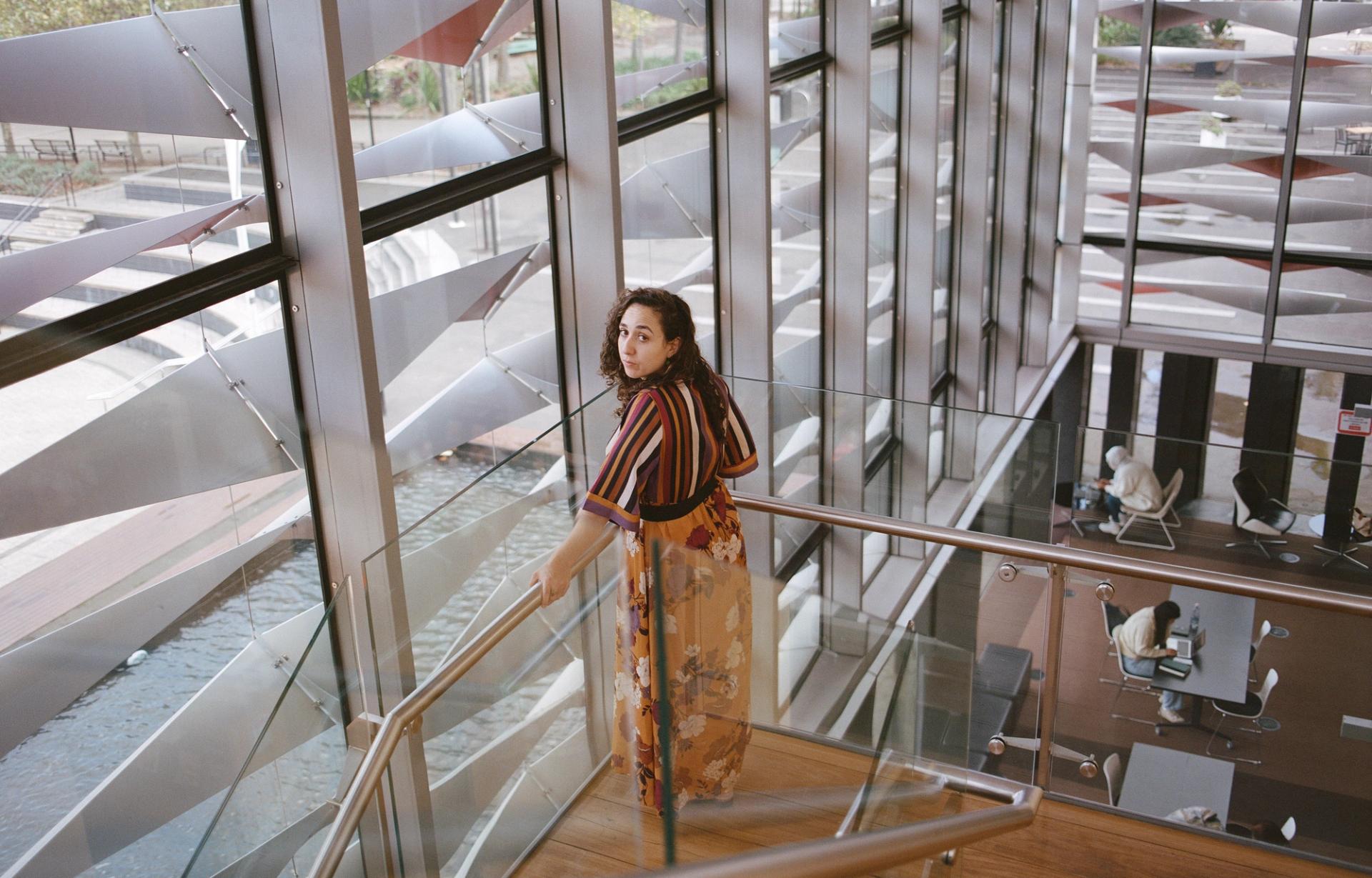 Person looks behind them at the camera, while standing amongst a glass framed staircase.