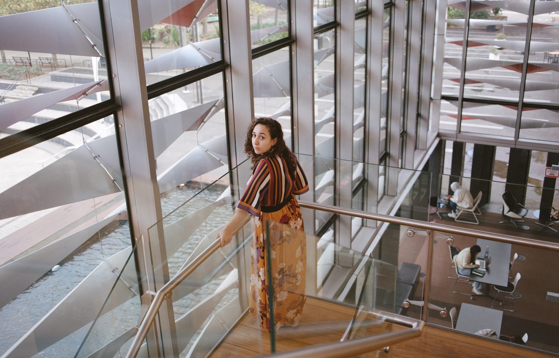Person looks behind them at the camera, while standing amongst a glass framed staircase.