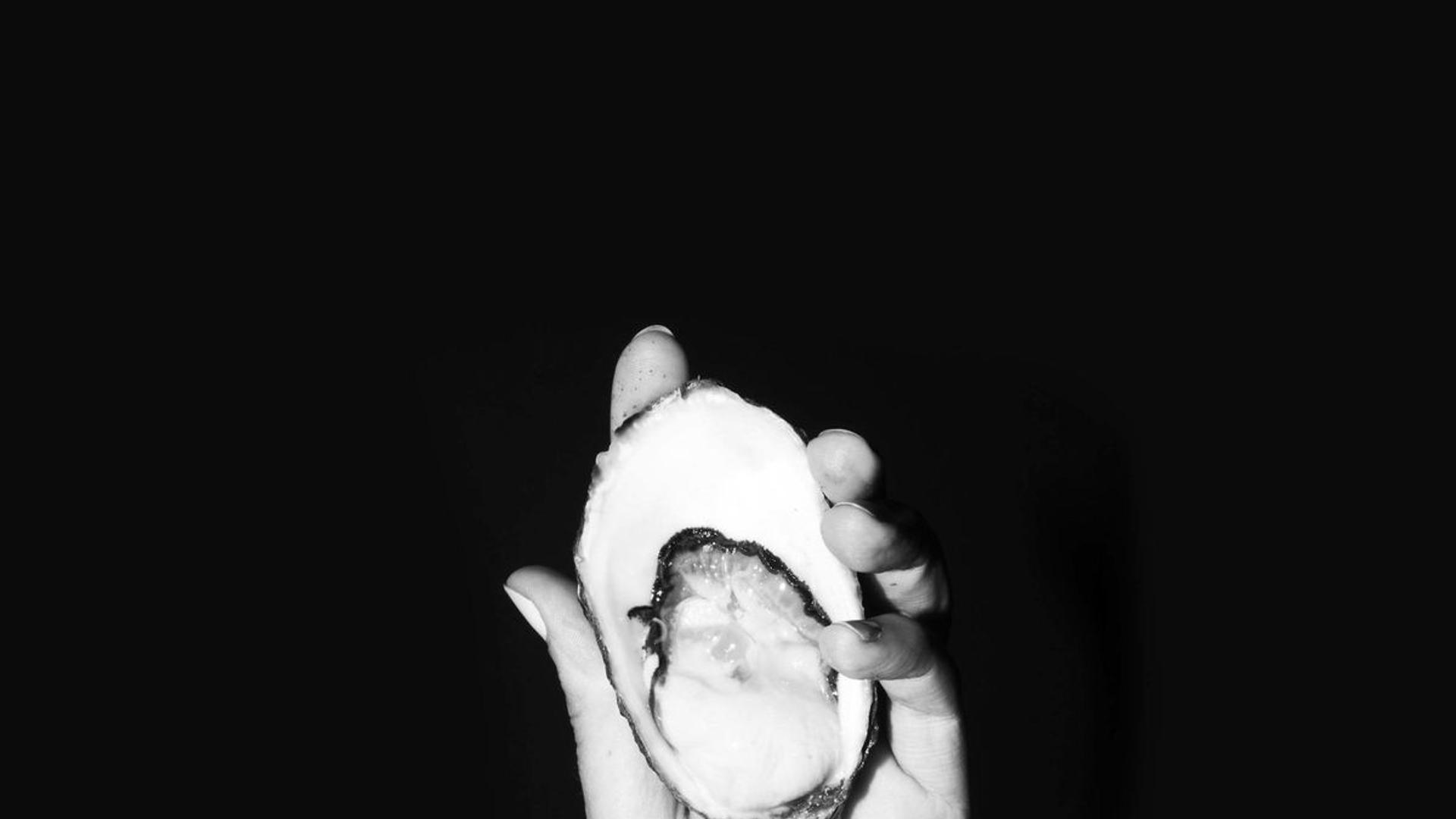 A hand holds an open oyster.