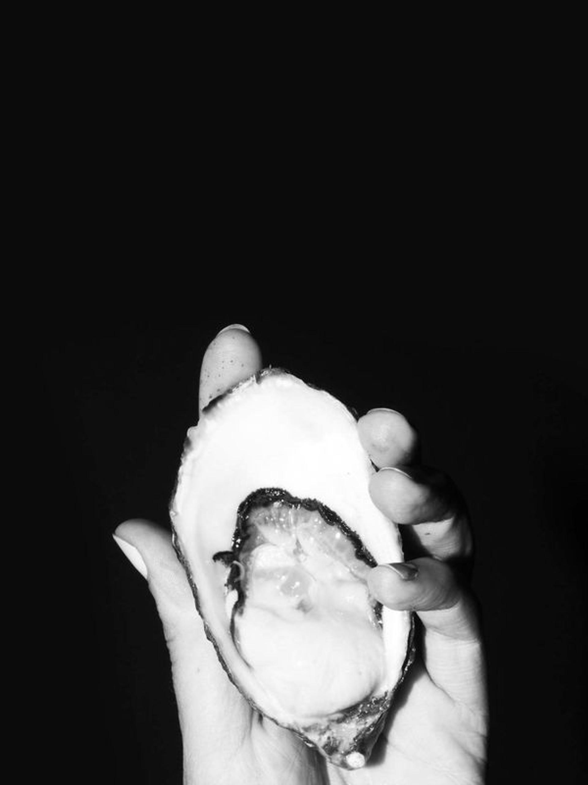 A hand holds an open oyster.