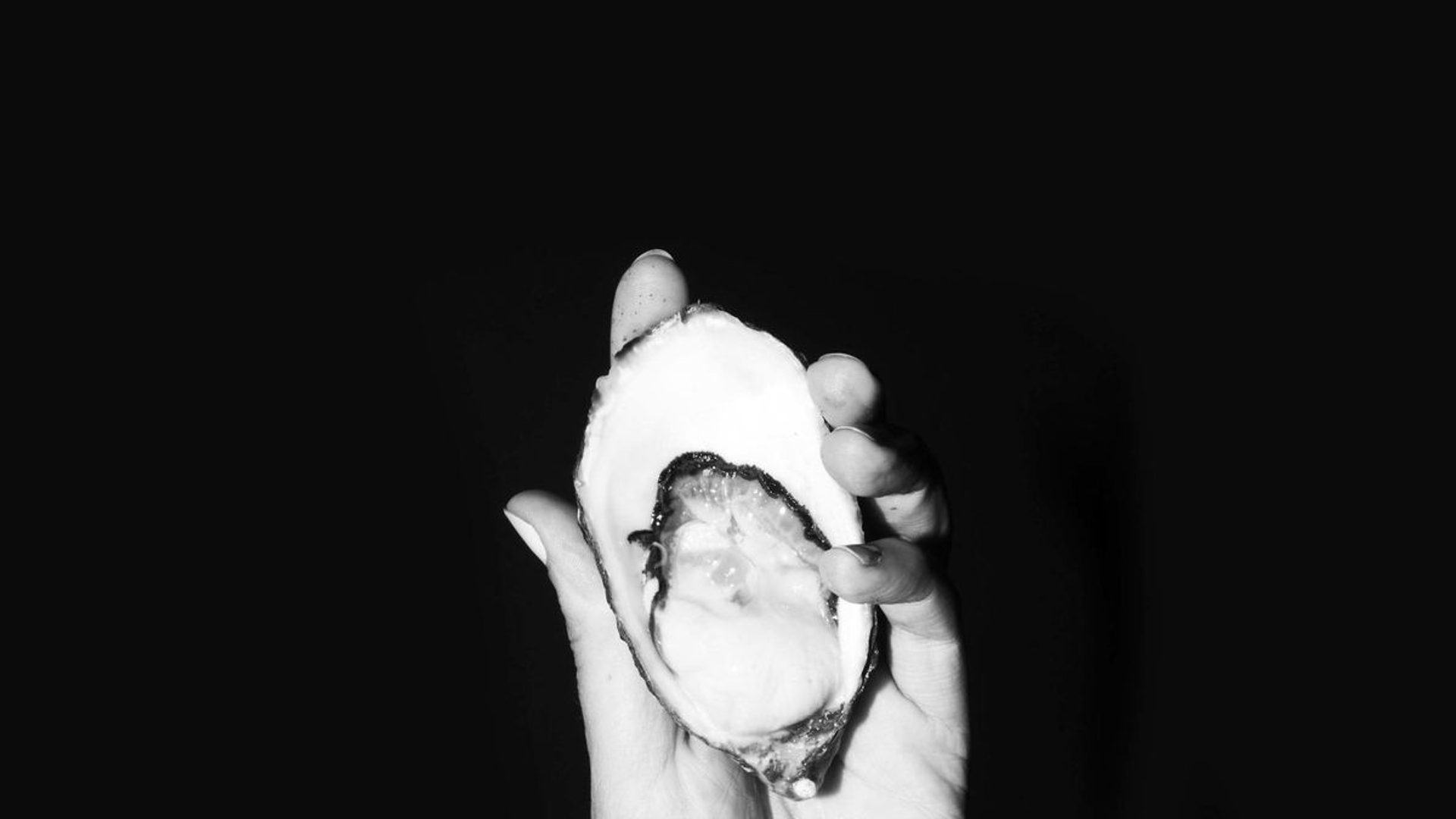 A hand holds an open oyster.