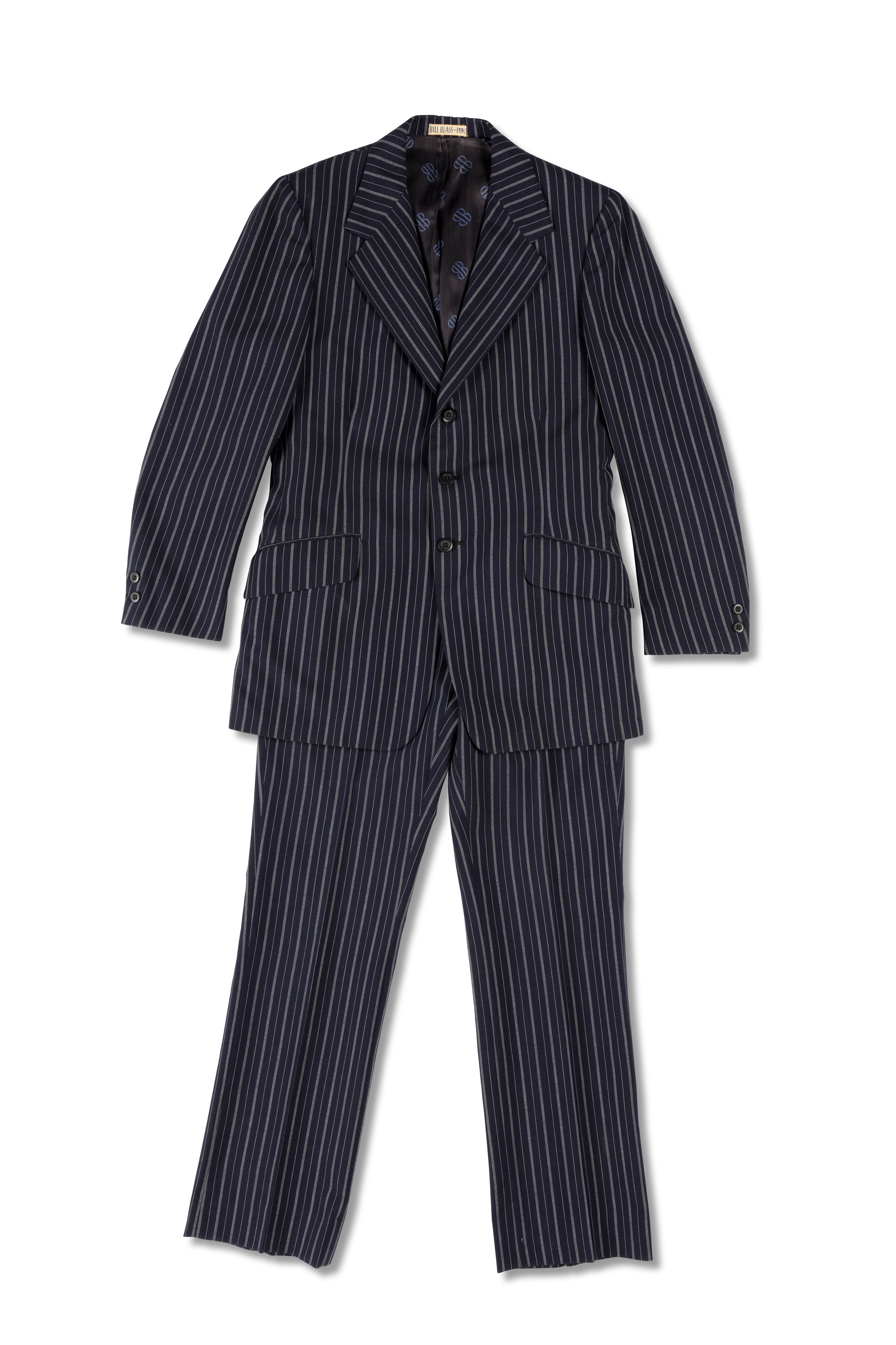 A navy blue mens suit of a blazer jacket and trousers made of wool pinstripped with white, it is partially lined with blue monogrammed polyester, the monogram 'BB' is in black. There is a centre back vent and a centre front opening fastening with three navy blue plastic buttons. At each cuff there are two small navy blue plastic buttons.