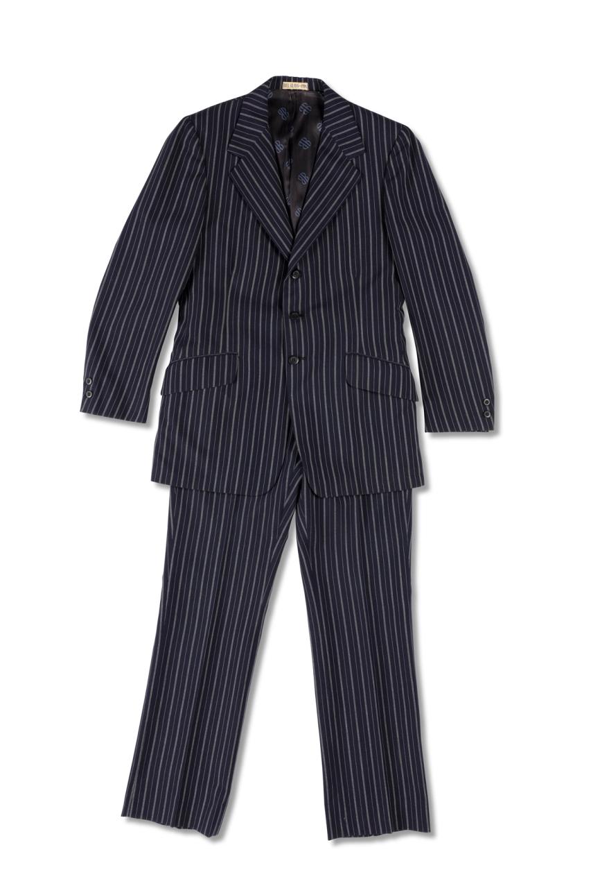 A navy blue mens suit of a blazer jacket and trousers made of wool pinstripped with white, it is partially lined with blue monogrammed polyester, the monogram 'BB' is in black. There is a centre back vent and a centre front opening fastening with three navy blue plastic buttons. At each cuff there are two small navy blue plastic buttons.
