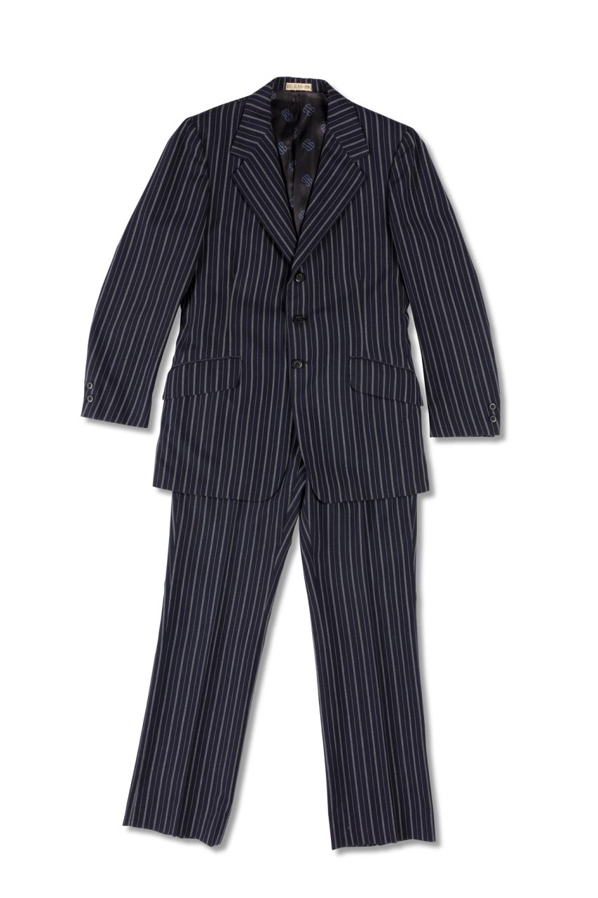 A navy blue mens suit of a blazer jacket and trousers made of wool pinstripped with white, it is partially lined with blue monogrammed polyester, the monogram 'BB' is in black. There is a centre back vent and a centre front opening fastening with three navy blue plastic buttons. At each cuff there are two small navy blue plastic buttons.