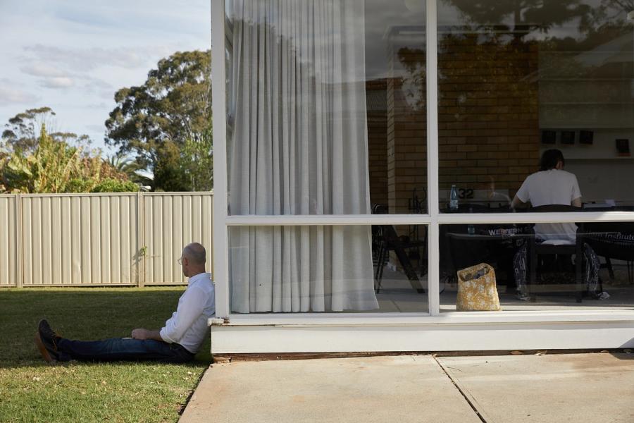 Figure leans on house exterior while sitting on grass