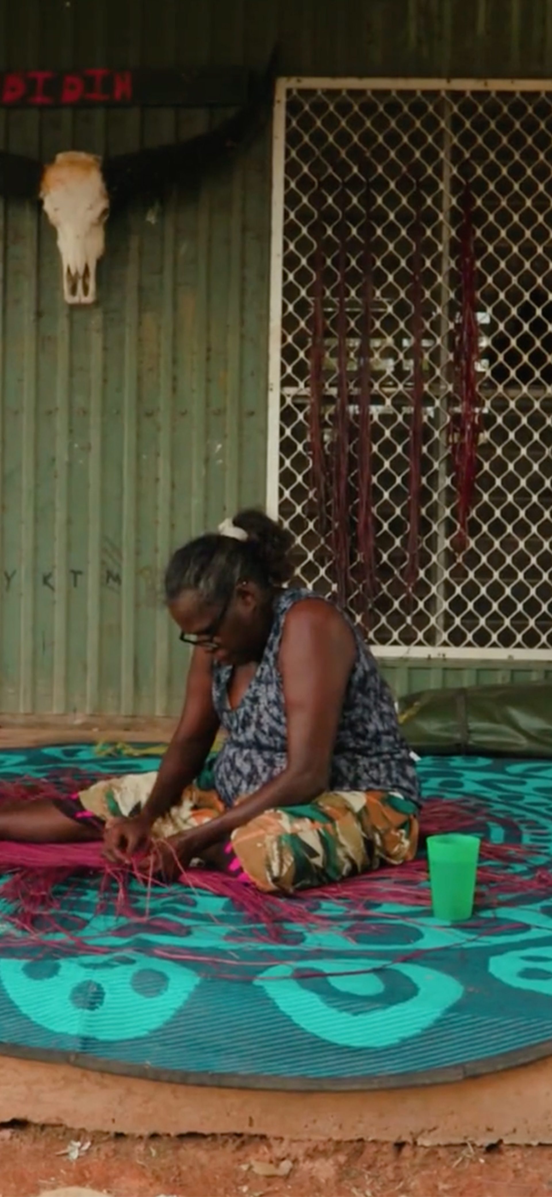 Women touching a traditionally woven mat on atop fabric on the floor.