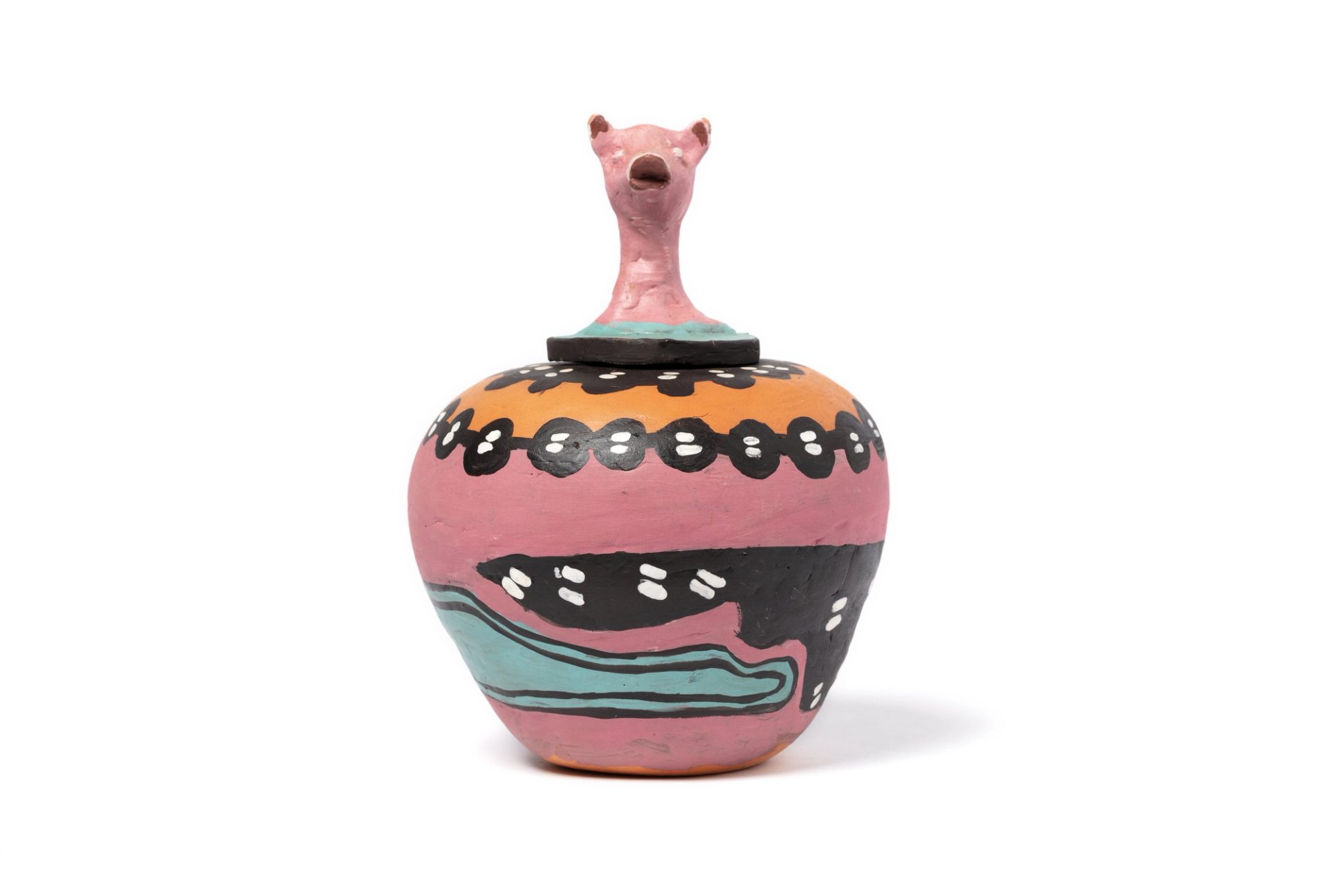 A round hand-formed pot in thick clay with a sculpted lid representing the head of a pig. Around the base is a painted pink ground, black and aqua forms, and white paint applied in the 'dot painting' style. The interior is glazed. Accompanying the pot is a folded, beige cardboard label. The label reads 'Hermannsburg Potters, 'My Pig Is Looking for Food', entirely hand crafted and painted by the Aranda people from Hermannsburg, Central Australia, Irene Entata.
