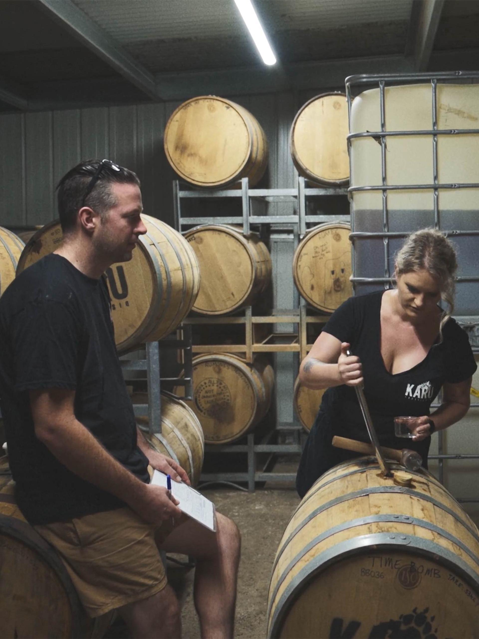 Two people in a room of wooden barrels, looking down at one.
