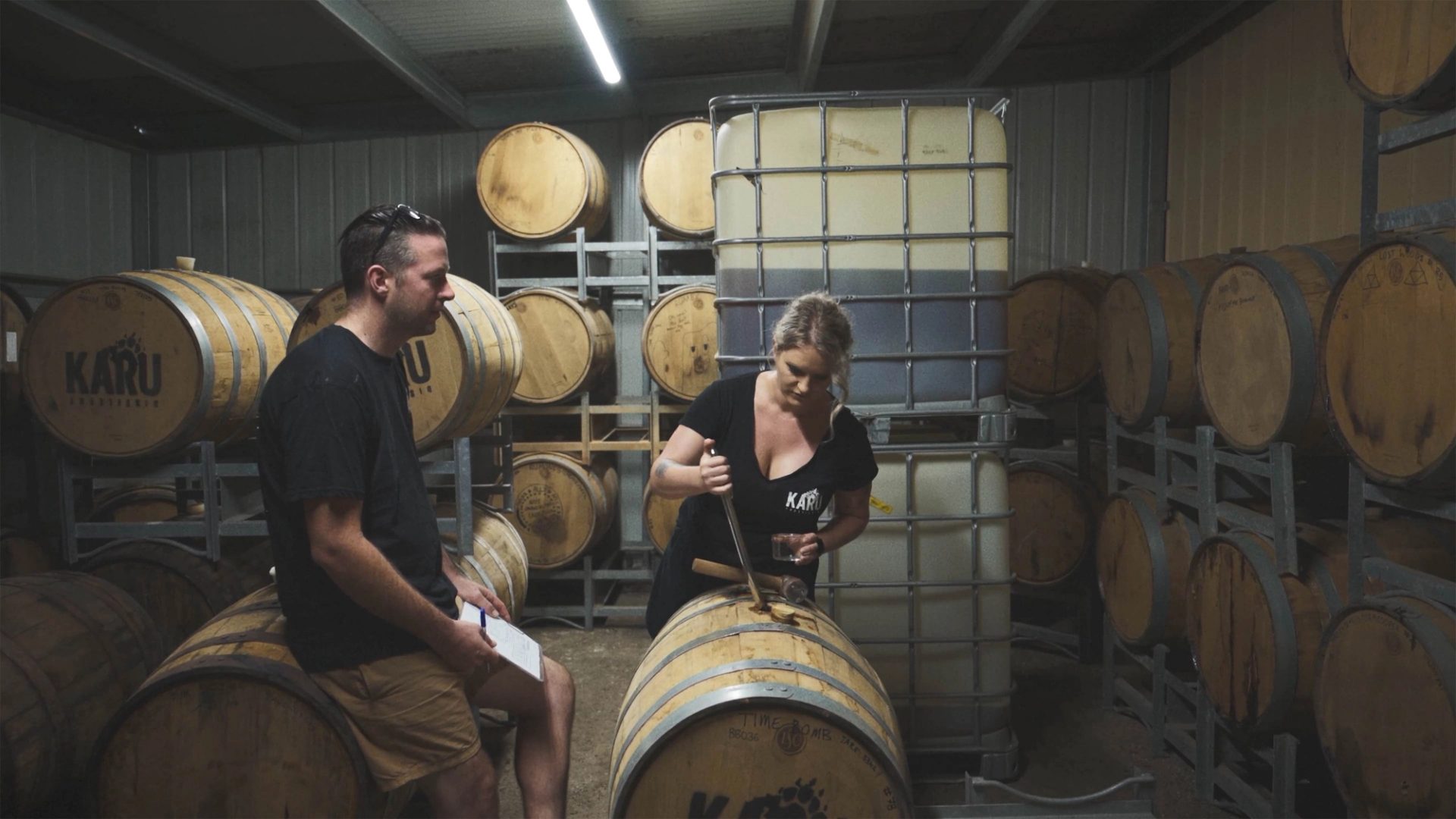 Two people in a room of wooden barrels, looking down at one.