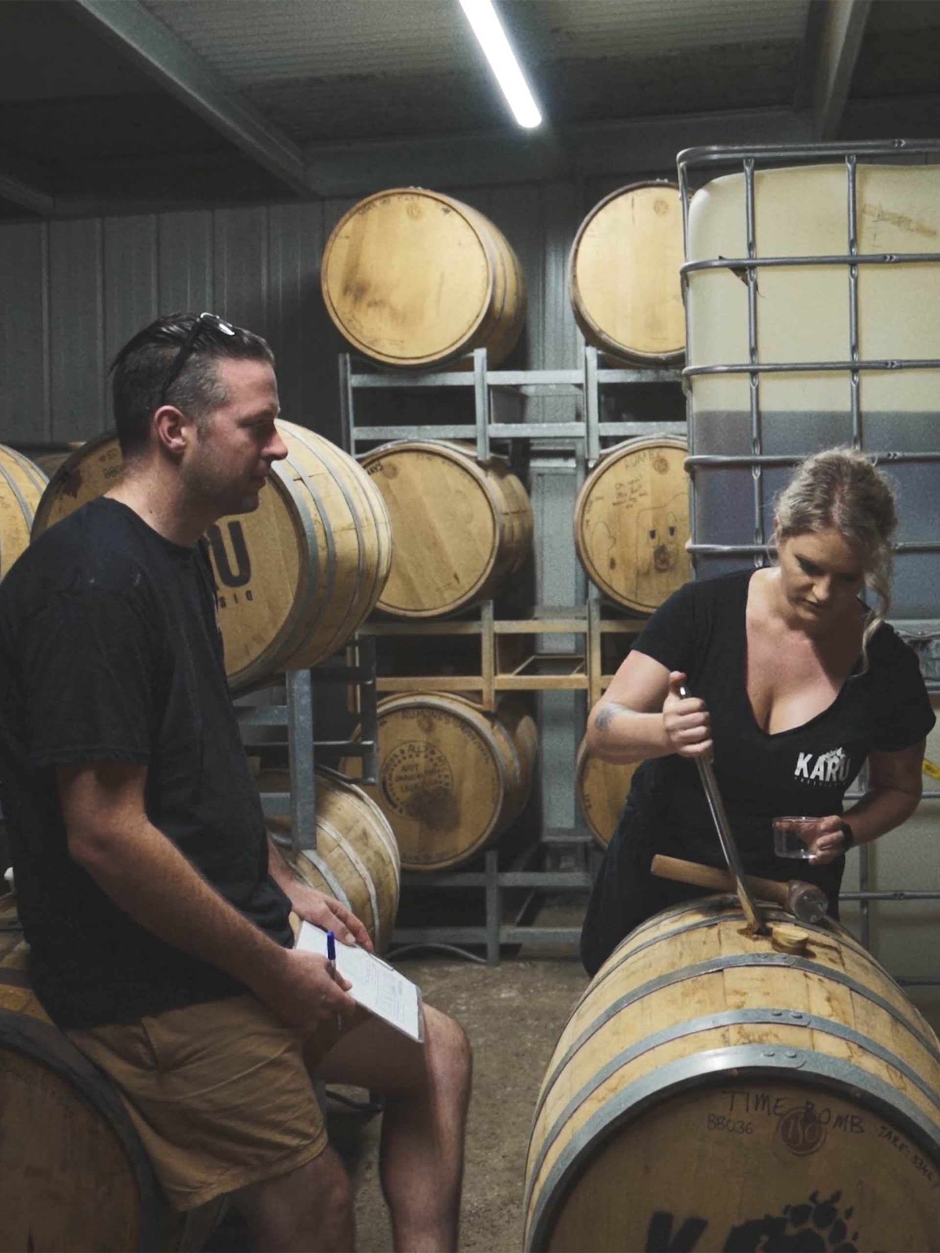 Two people in a room of wooden barrels, looking down at one.