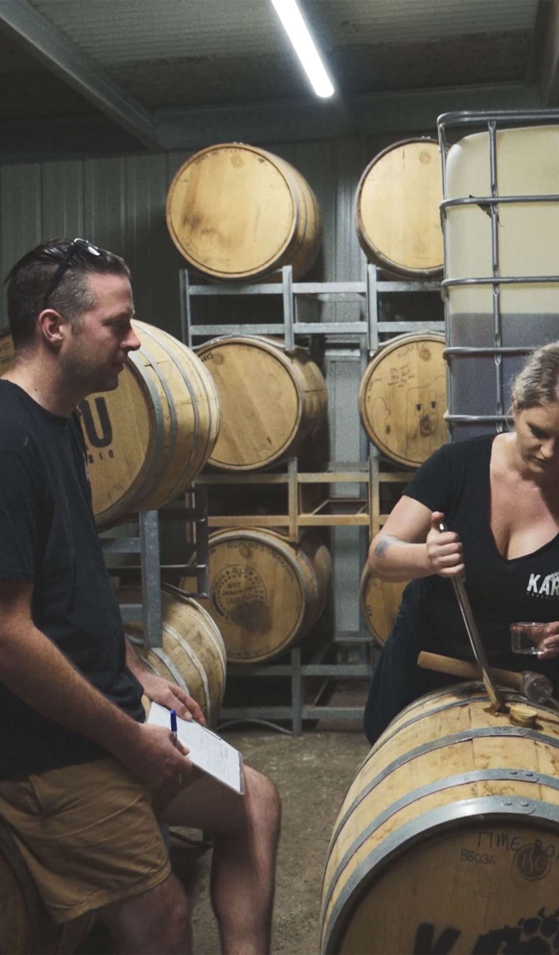 Two people in a room of wooden barrels, looking down at one.