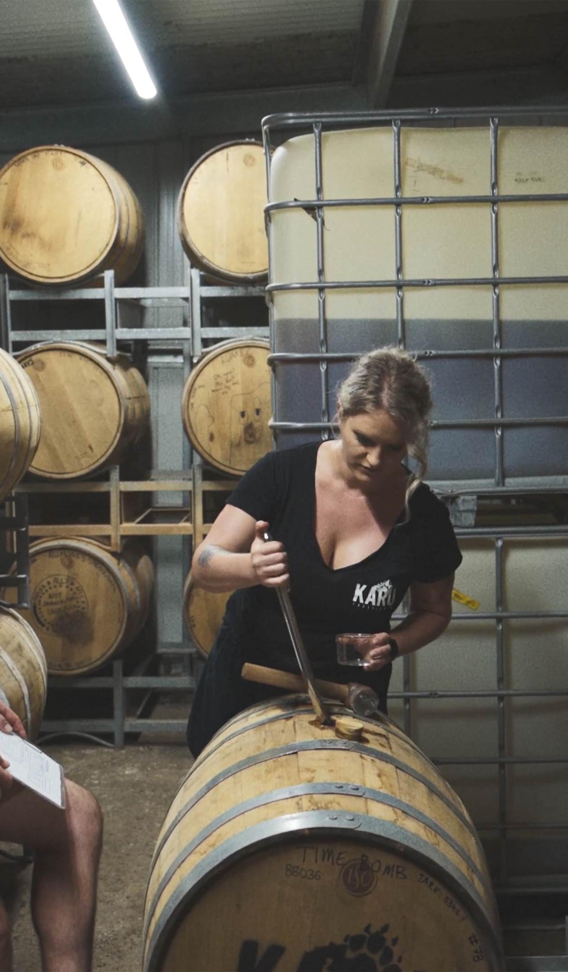 Two people in a room of wooden barrels, looking down at one.
