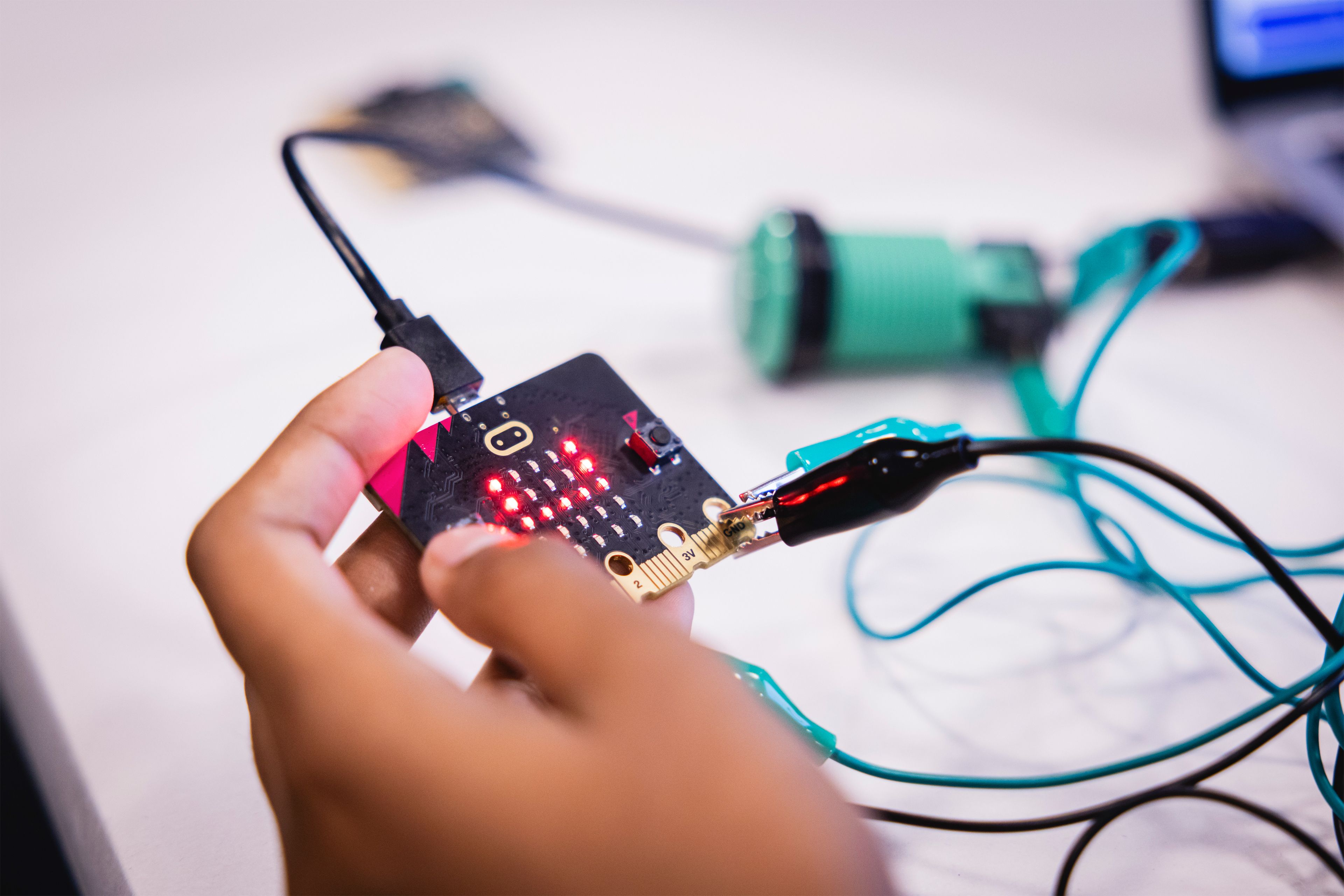 Close-up photo of a student holding a micro-bit board, multiple wires connected to it.