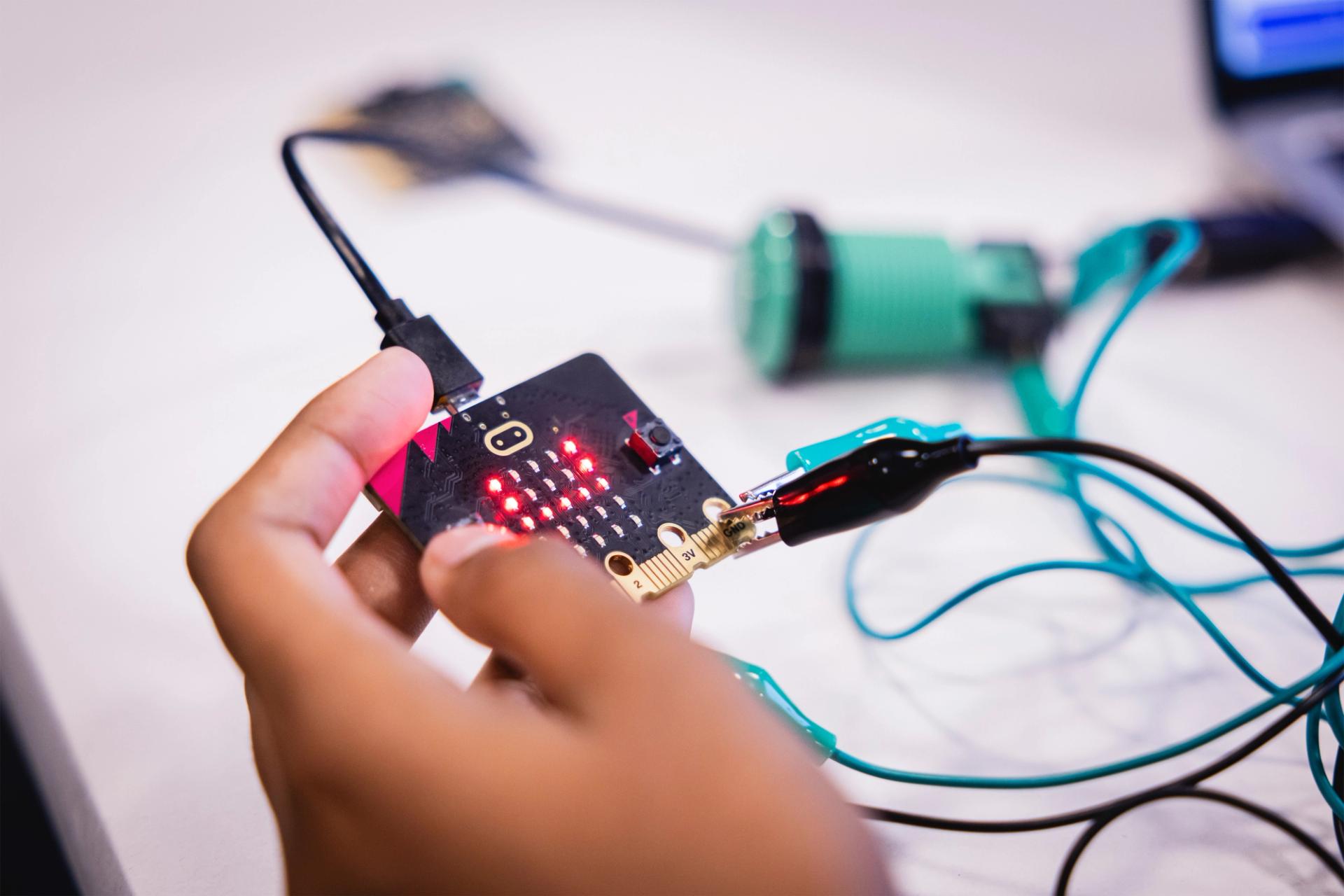 Close-up photo of a student holding a micro-bit board, multiple wires connected to it.