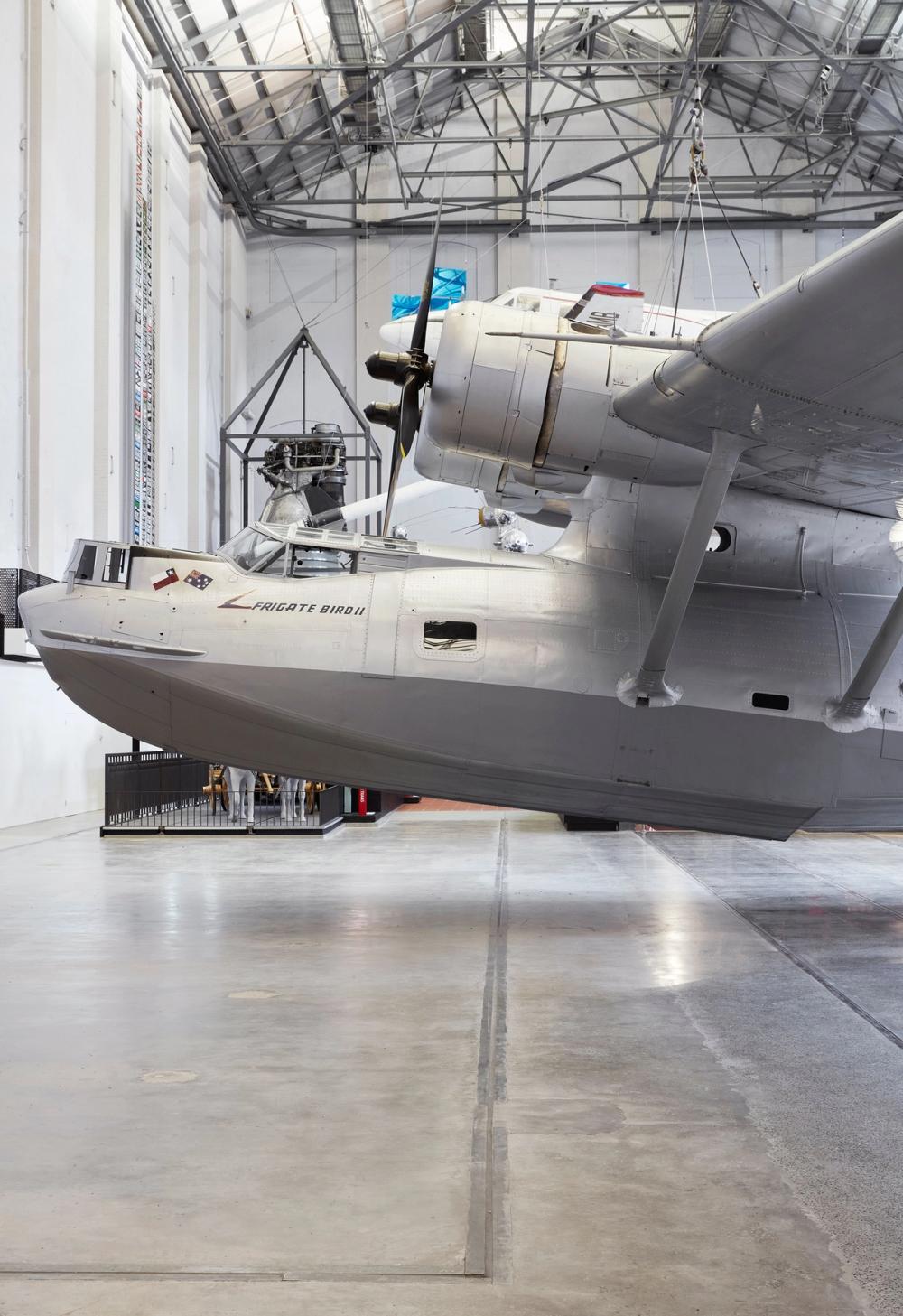 Nose and left propeller of silver plane Catalina Frigate Bird II suspended above the floor.