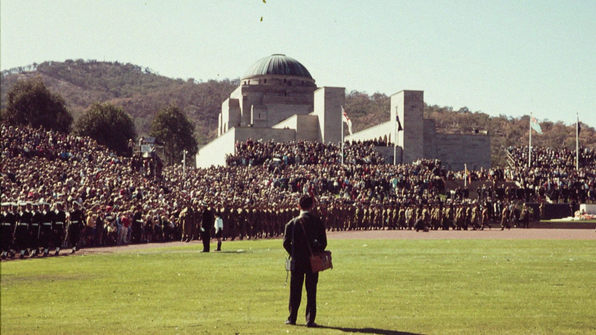 Man standing in field surrounded by those in uniforms.