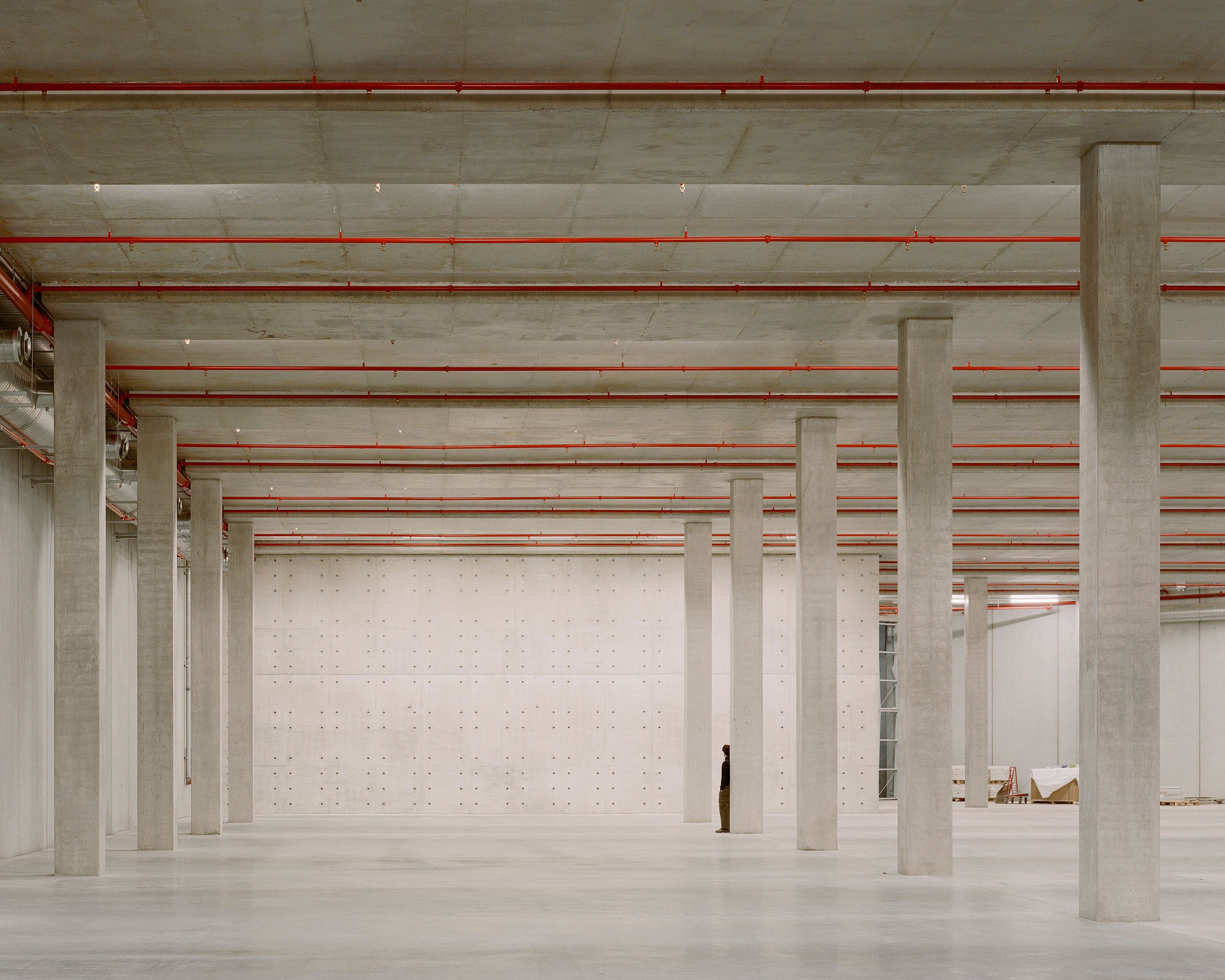 Concrete pillars inside an empty exhibition space, with a person for scale