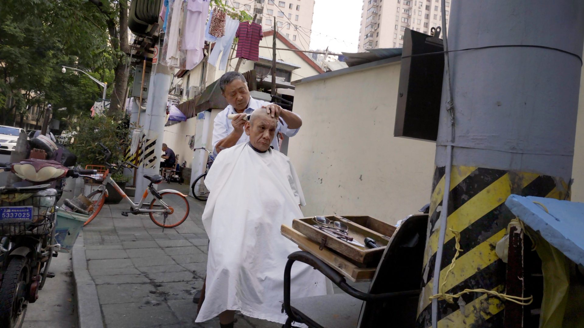 Two men in an urban streetscape having a haircut