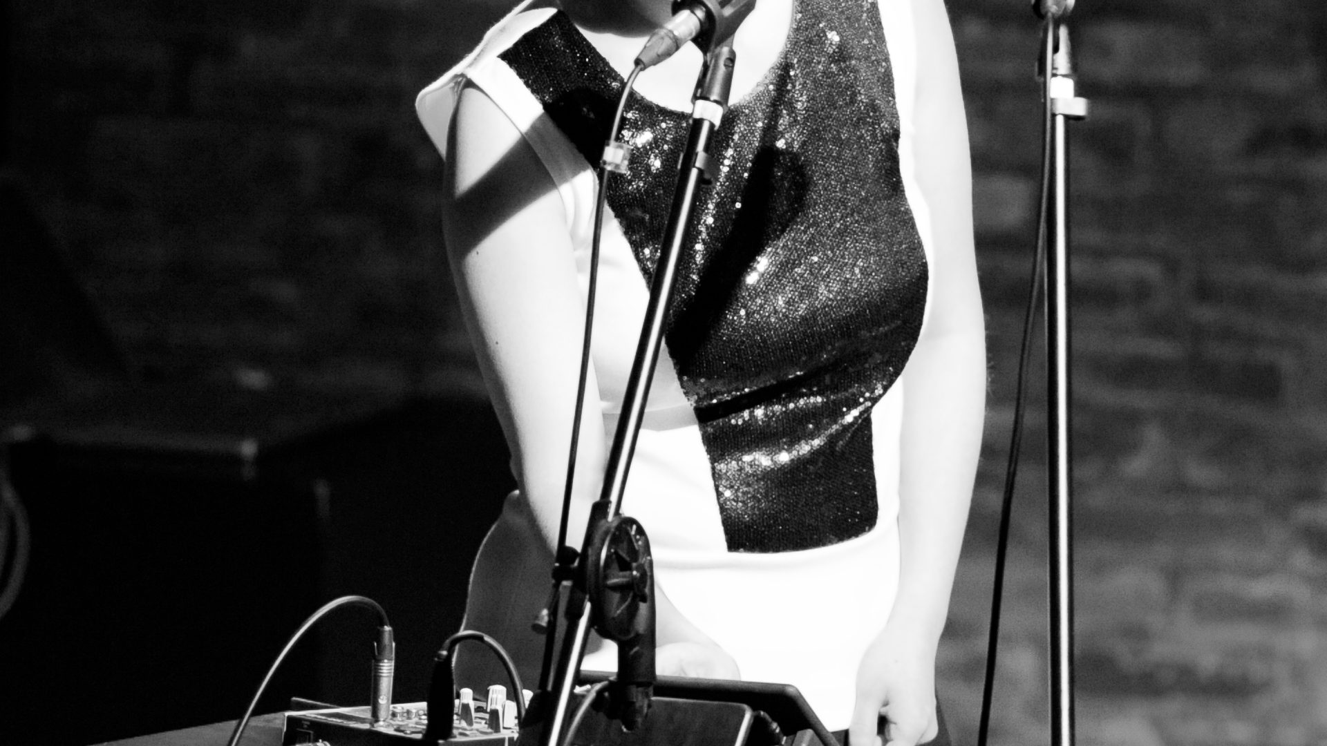 Black and white image of performer with bob hair in a black and white dress behind a microphone.