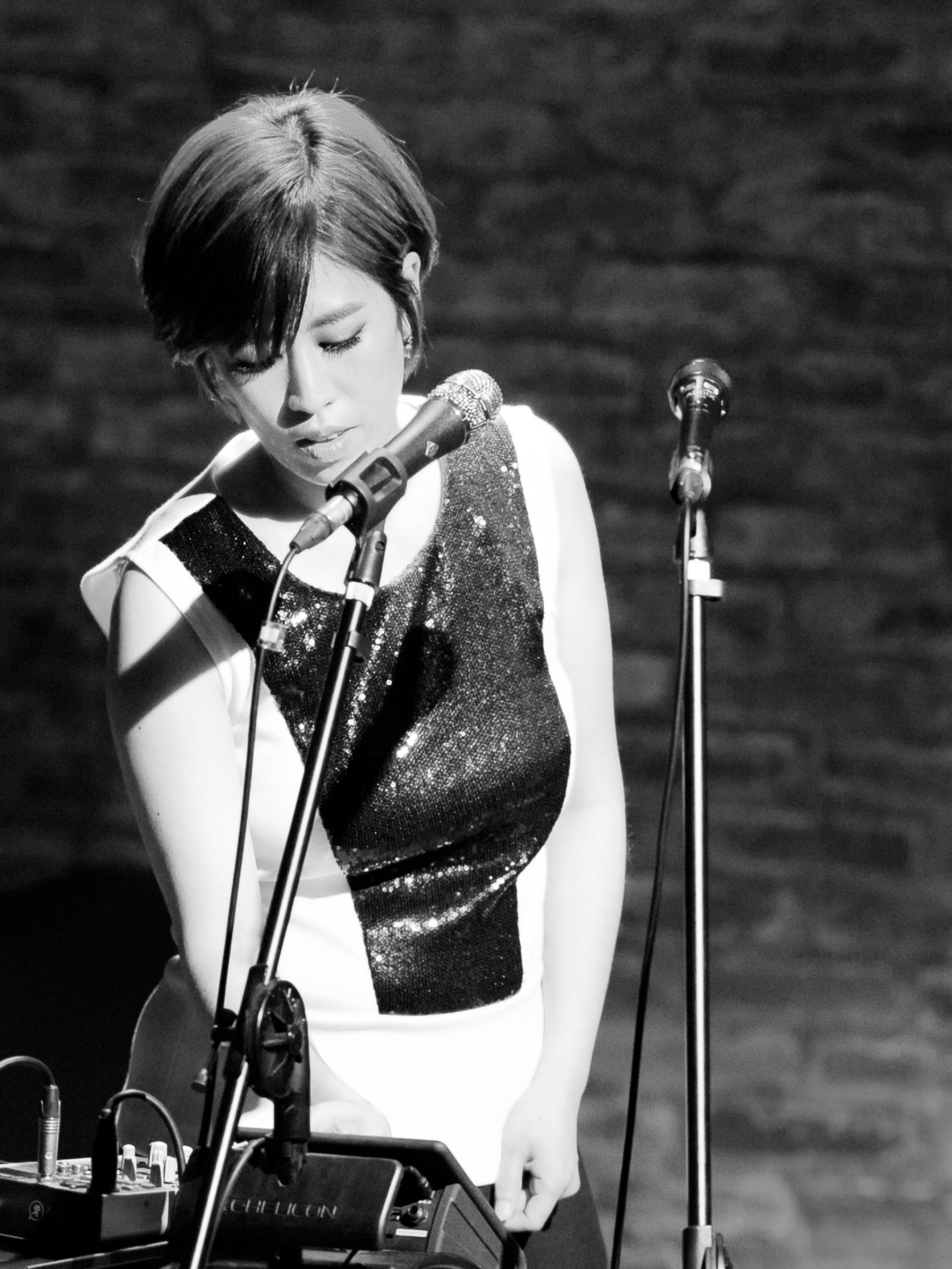 Black and white image of performer with bob hair in a black and white dress behind a microphone.