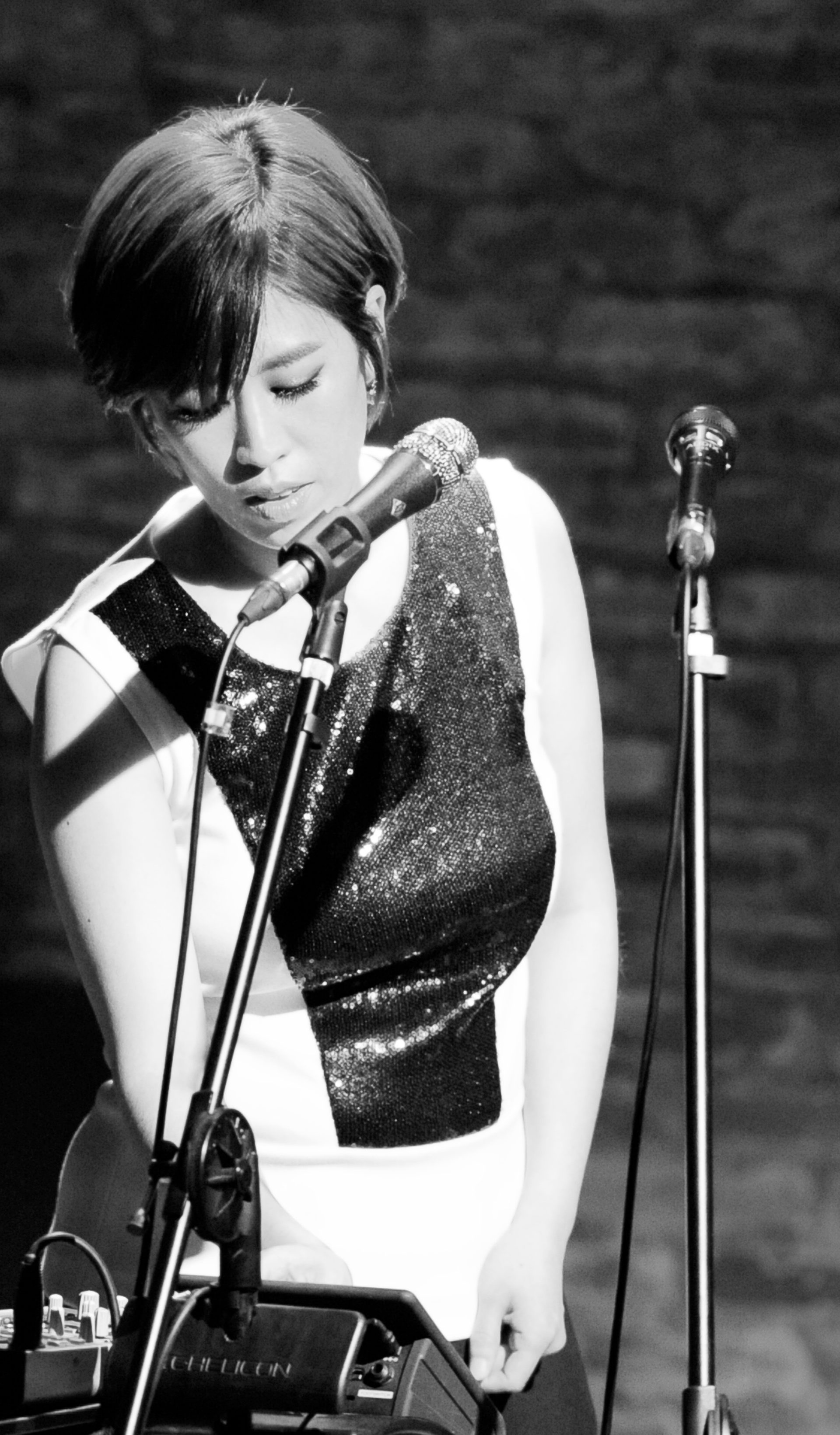 Black and white image of performer with bob hair in a black and white dress behind a microphone.