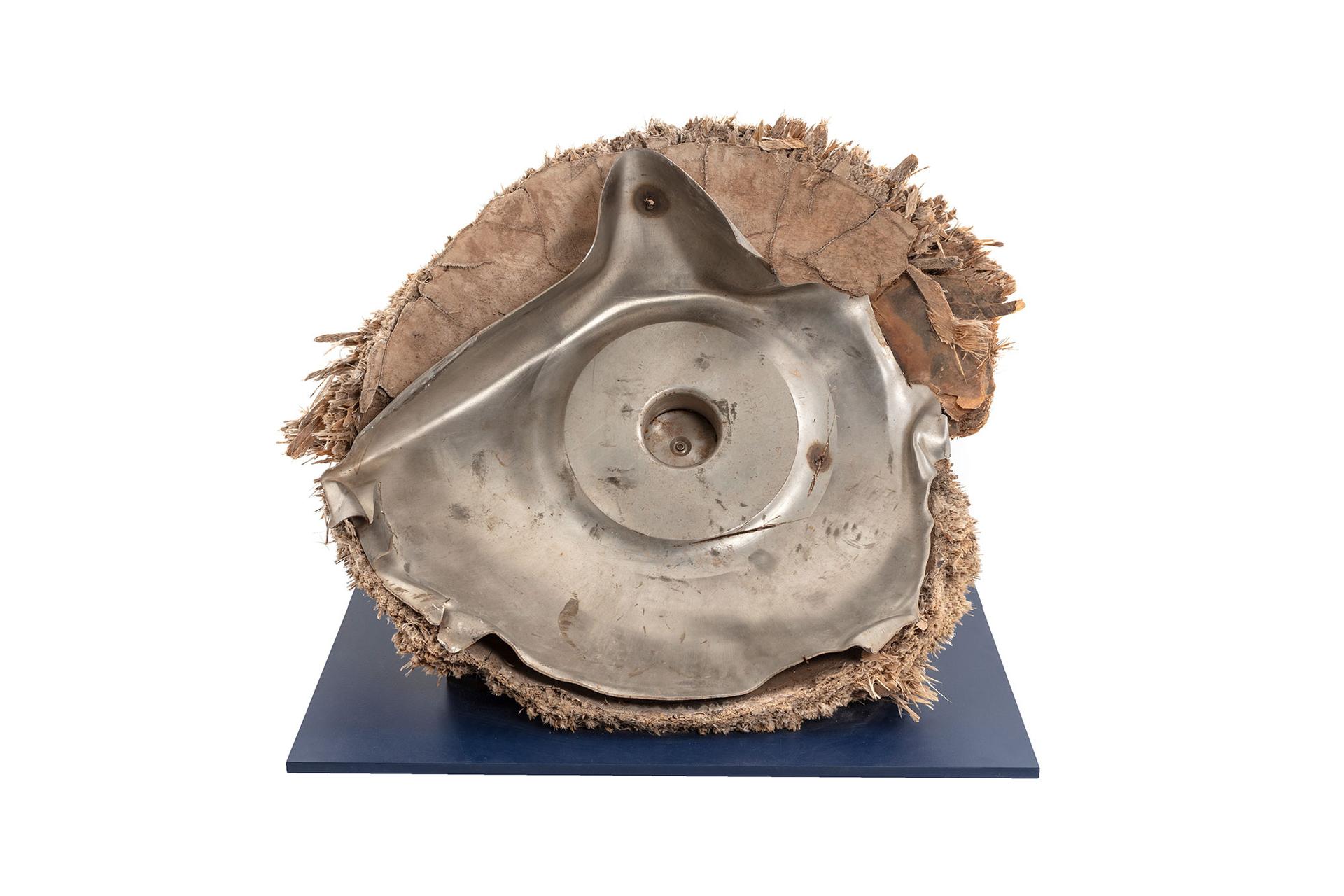Space debris, Skylab space station, titanium/fibreglass, McDonnell Douglas Astronautics Co, USA, 1970-1972. The fragment is the end cap from pressurised oxygen tank from the Skylab space station. Originally the end of an enclosed cylinder, the titanium tank structure is torn and bent as a result of the stresses that ripped it away from the rest of the vessel. The exterior is covered by a composite insulation material with a woven fibreglass outer surface. A circular lid, protruding above the external insulation, covers an access hatch to the tank. A black and red wire, possibly originally connected to an external power source or sensor, is attached to the lid.