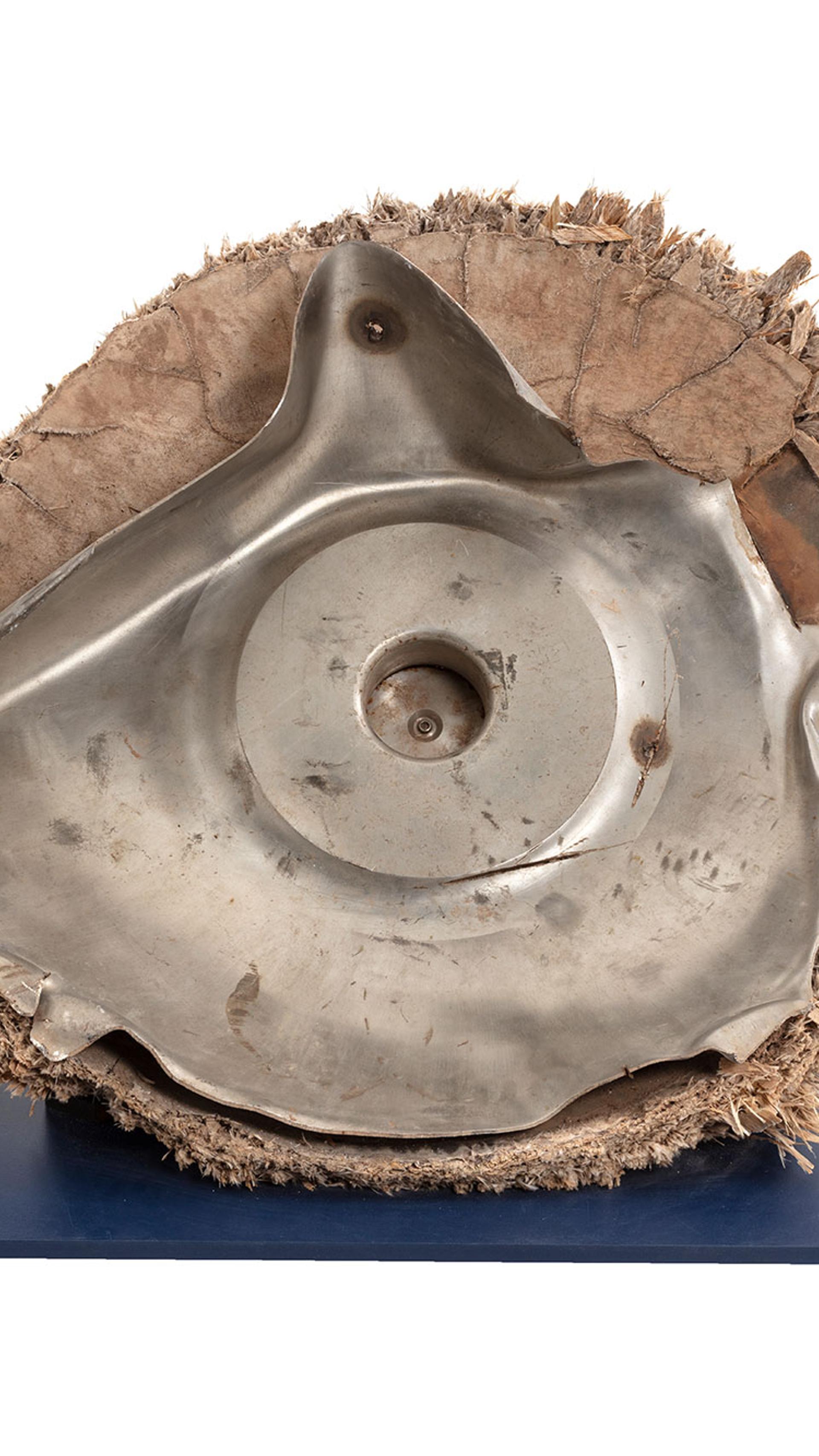 Space debris, Skylab space station, titanium/fibreglass, McDonnell Douglas Astronautics Co, USA, 1970-1972. The fragment is the end cap from pressurised oxygen tank from the Skylab space station. Originally the end of an enclosed cylinder, the titanium tank structure is torn and bent as a result of the stresses that ripped it away from the rest of the vessel. The exterior is covered by a composite insulation material with a woven fibreglass outer surface. A circular lid, protruding above the external insulation, covers an access hatch to the tank. A black and red wire, possibly originally connected to an external power source or sensor, is attached to the lid.