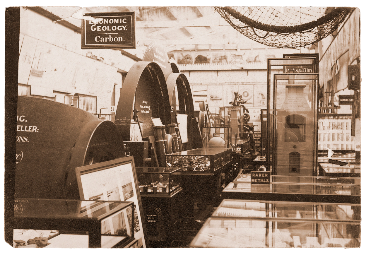 Sepia photograph of a crowed museum display with furnaces to the left and glass cabinets to the right