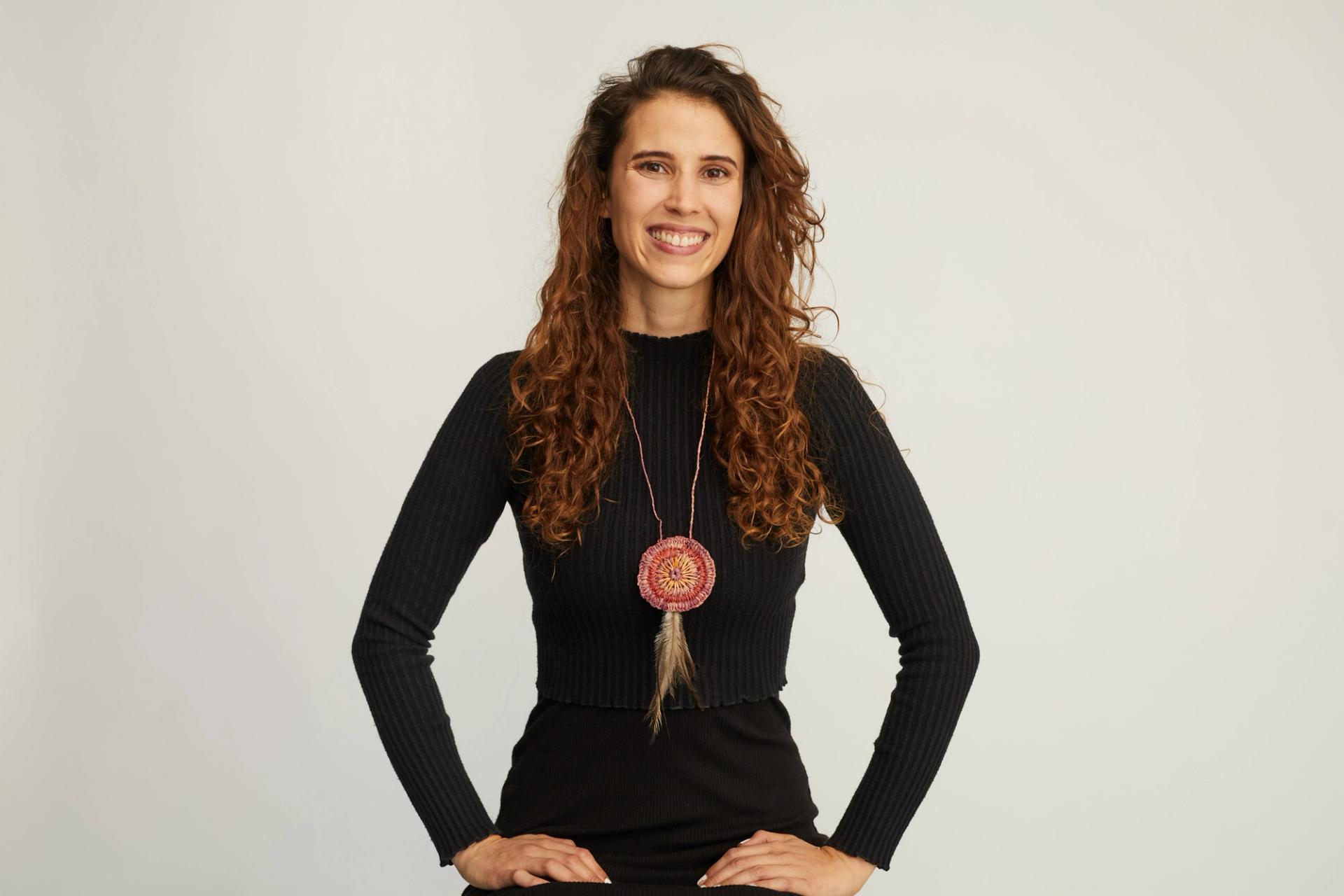 Women wearing all black clothing and a first nations necklace smiles at the camera.