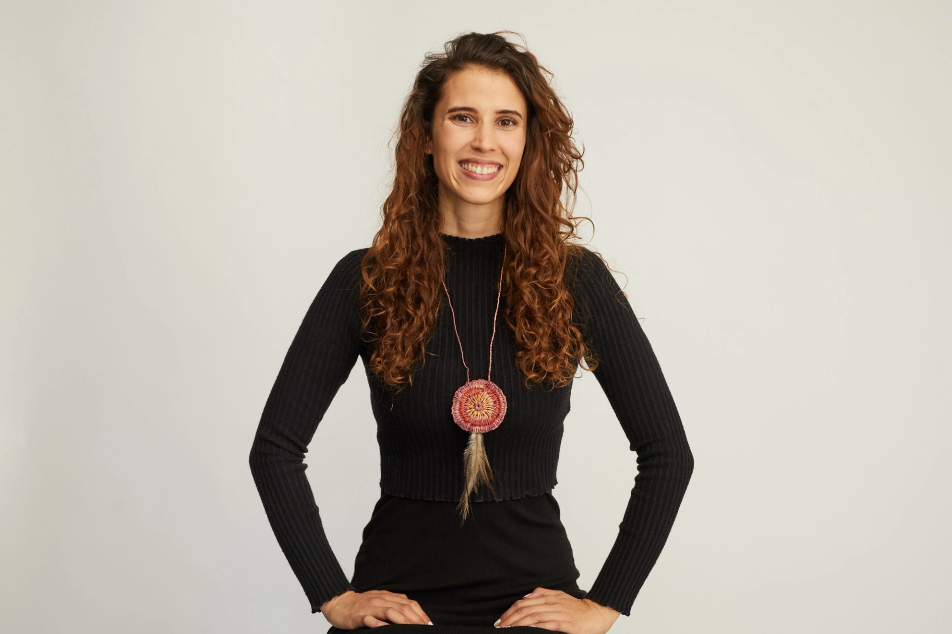 Women wearing all black clothing and a first nations necklace smiles at the camera.