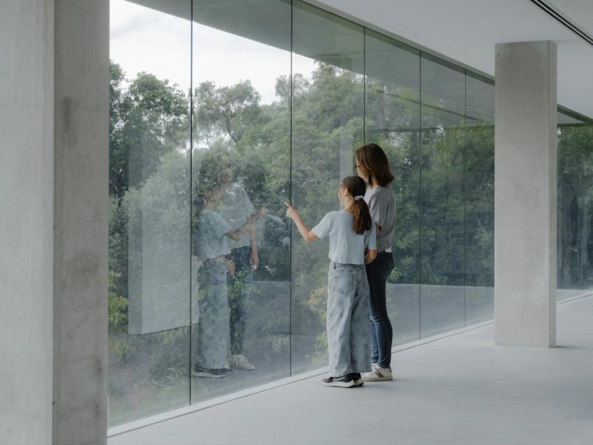 An adult and child looking outside a large scale floor to ceiling window.