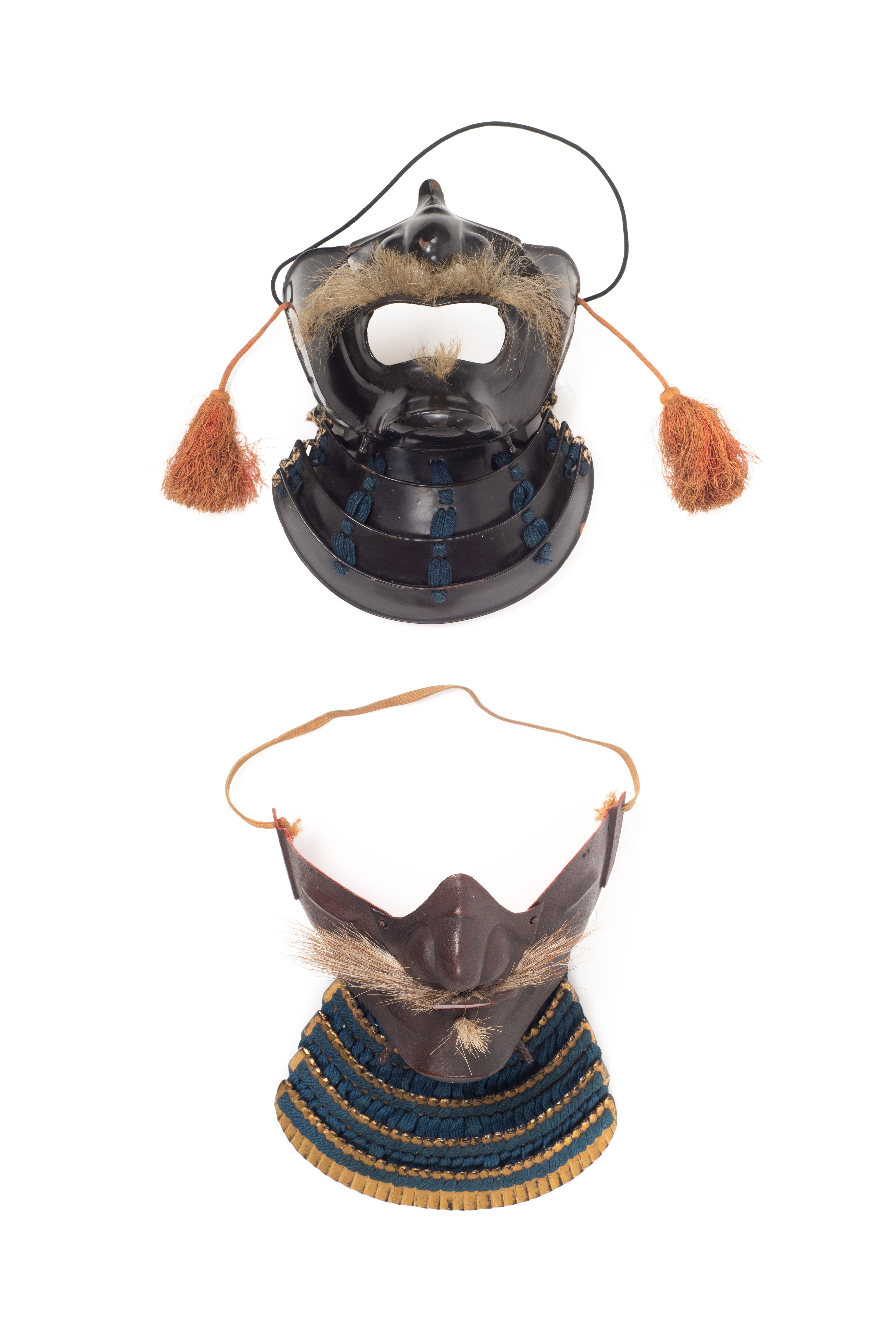 Two masks as Japanese facial armour (Mempō). One mask features a blue fabric cordage neck guard, or Yodare-kake, chin, cheek and nose armour and a horse hair moustache and small beard tuft. The second mask features a highly lacquered leather Yodare-kake with blue cordage and highly lacquered chin, cheek and nose armour, with a large mouth opening, a horse hair moustache and beard tuft and tassels, or Agemaki attached to each cheek guard.