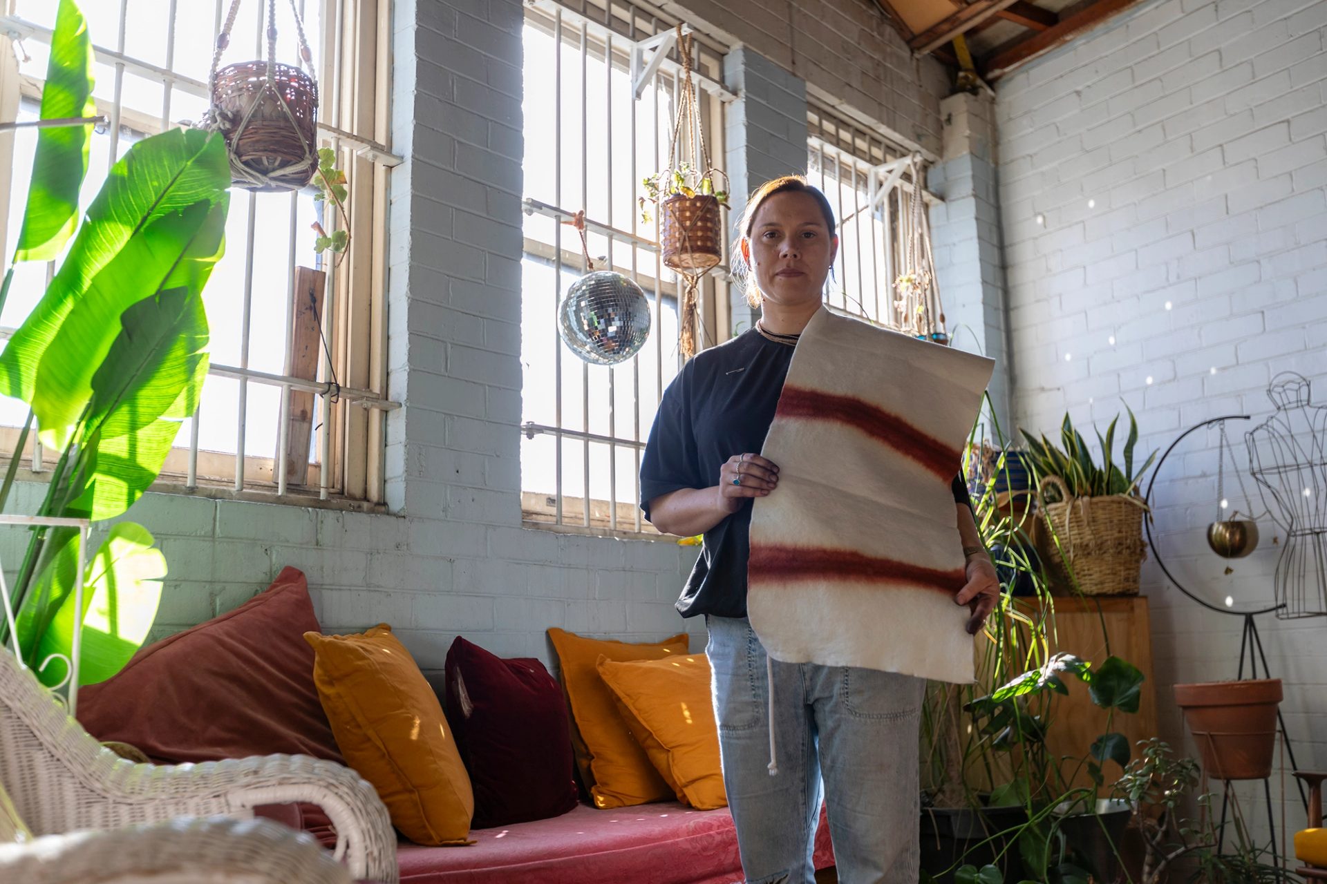 A woman holding a piece of textile, in a brick wall room, with windows behind.