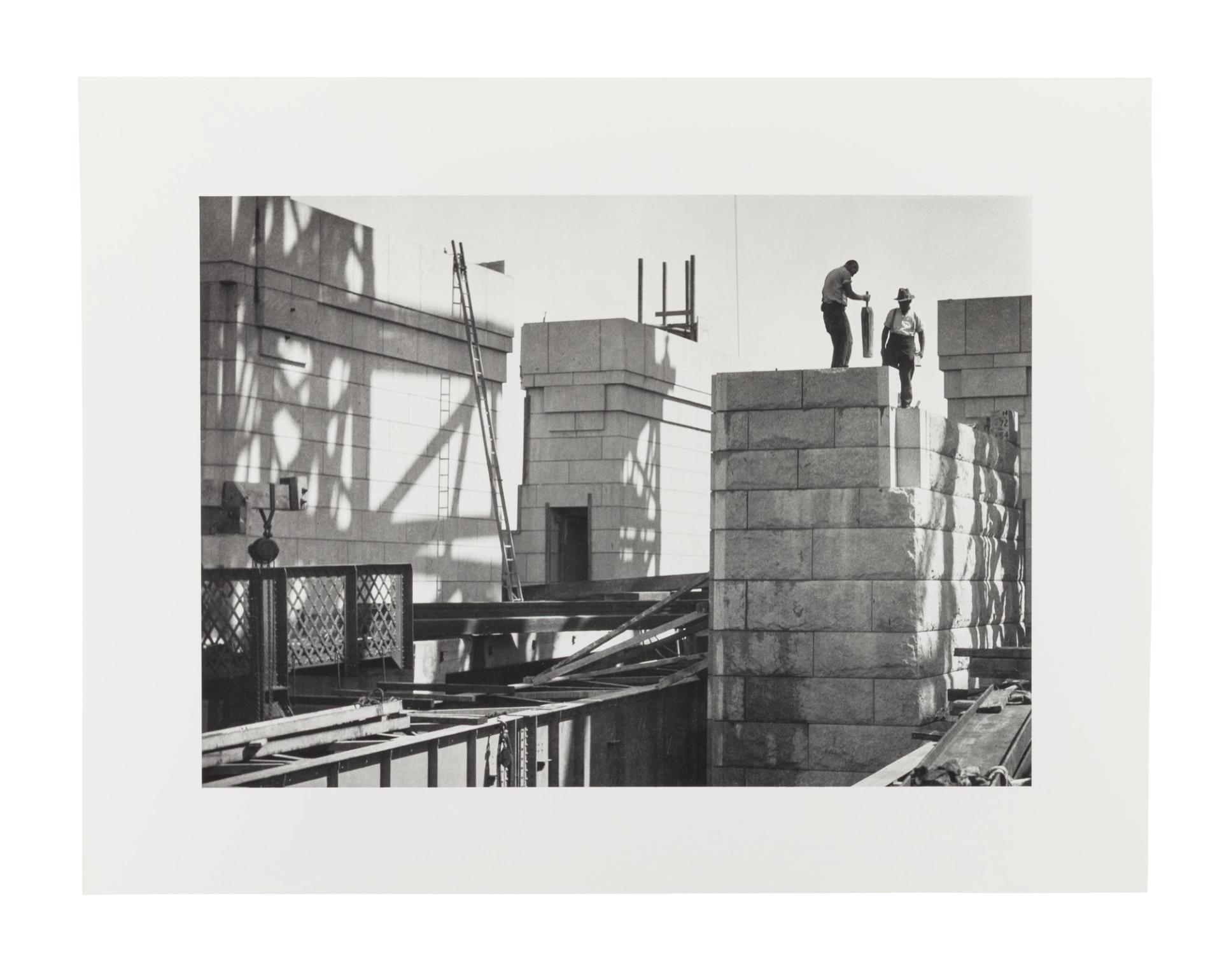 Image of two men working on the sandstone pylons of the Sydney Harbour Bridge. They stand on top of the pylon on the right side of the image.