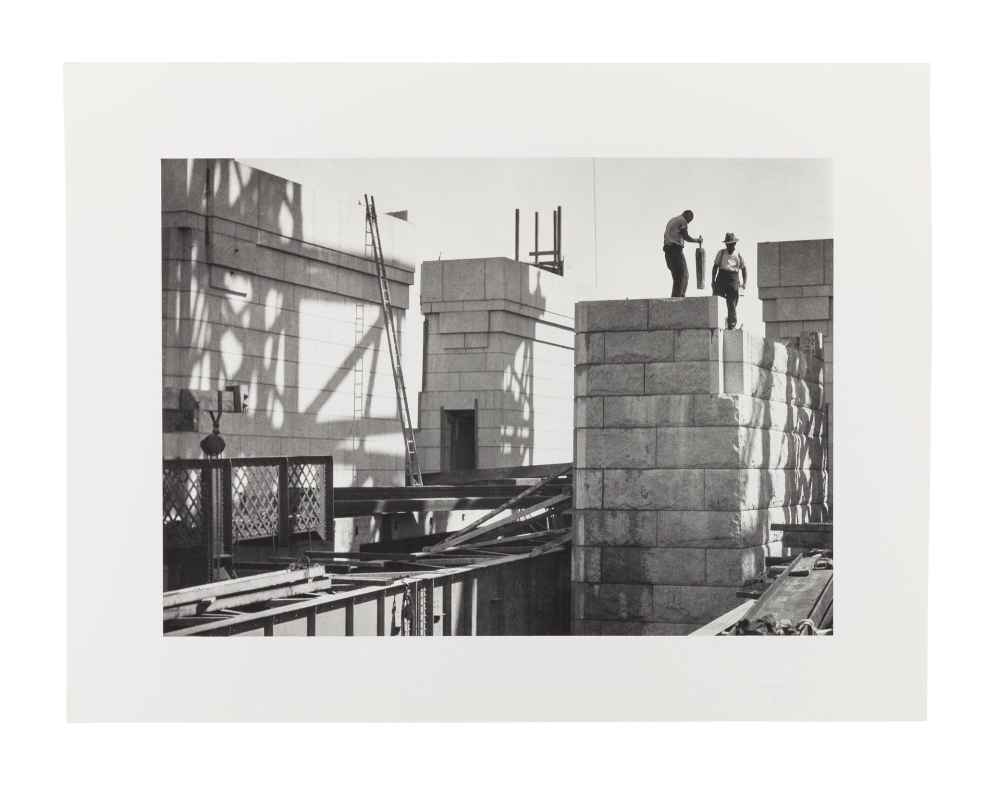 Image of two men working on the sandstone pylons of the Sydney Harbour Bridge. They stand on top of the pylon on the right side of the image.