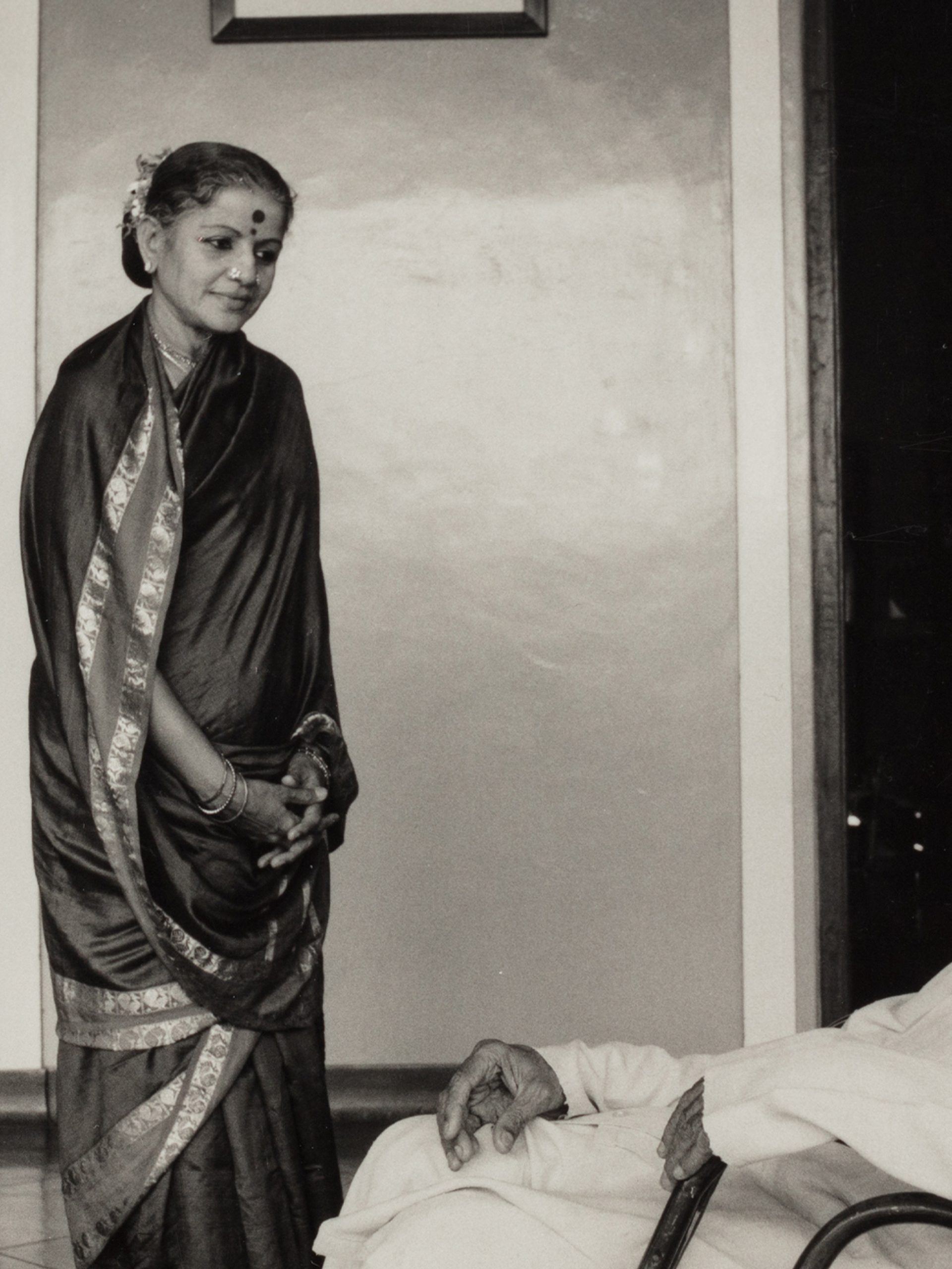 Black and white photograph depicting a woman (Subbulakshmi) wearing a sari looking down at a man (her husband T. Sadasivam) seated.