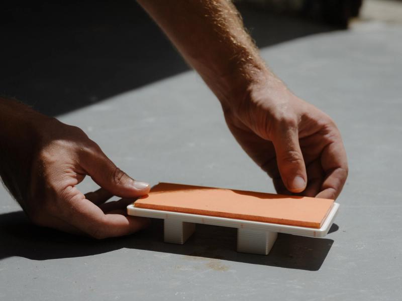 Tiny model of daybed being placed in the sun by two hands.