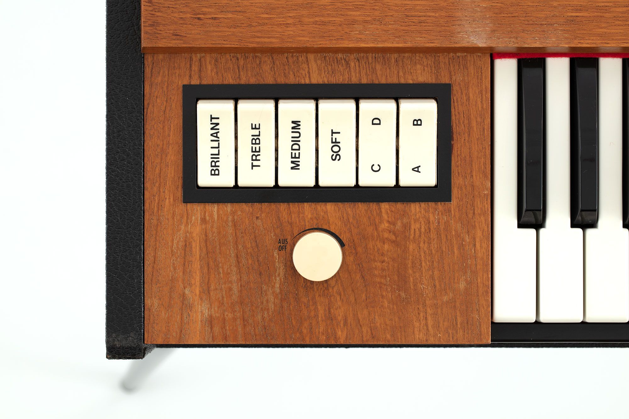Detail of the end of a timber keyboard showing a white dial and a series of white buttons with black text reading ‘brilliant’, ‘treble’, ‘medium’, ‘soft’, ‘c, d’, ‘a, b’.