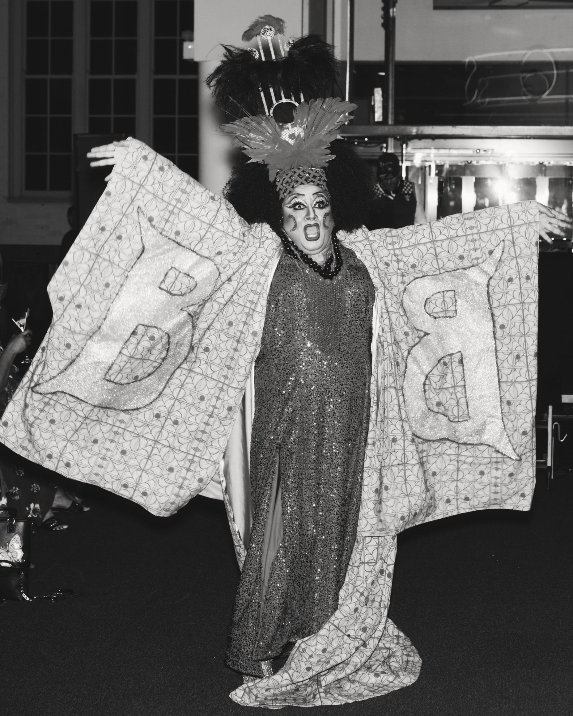 A drag performer performing in a kimono embroidered with large text reading ‘B'