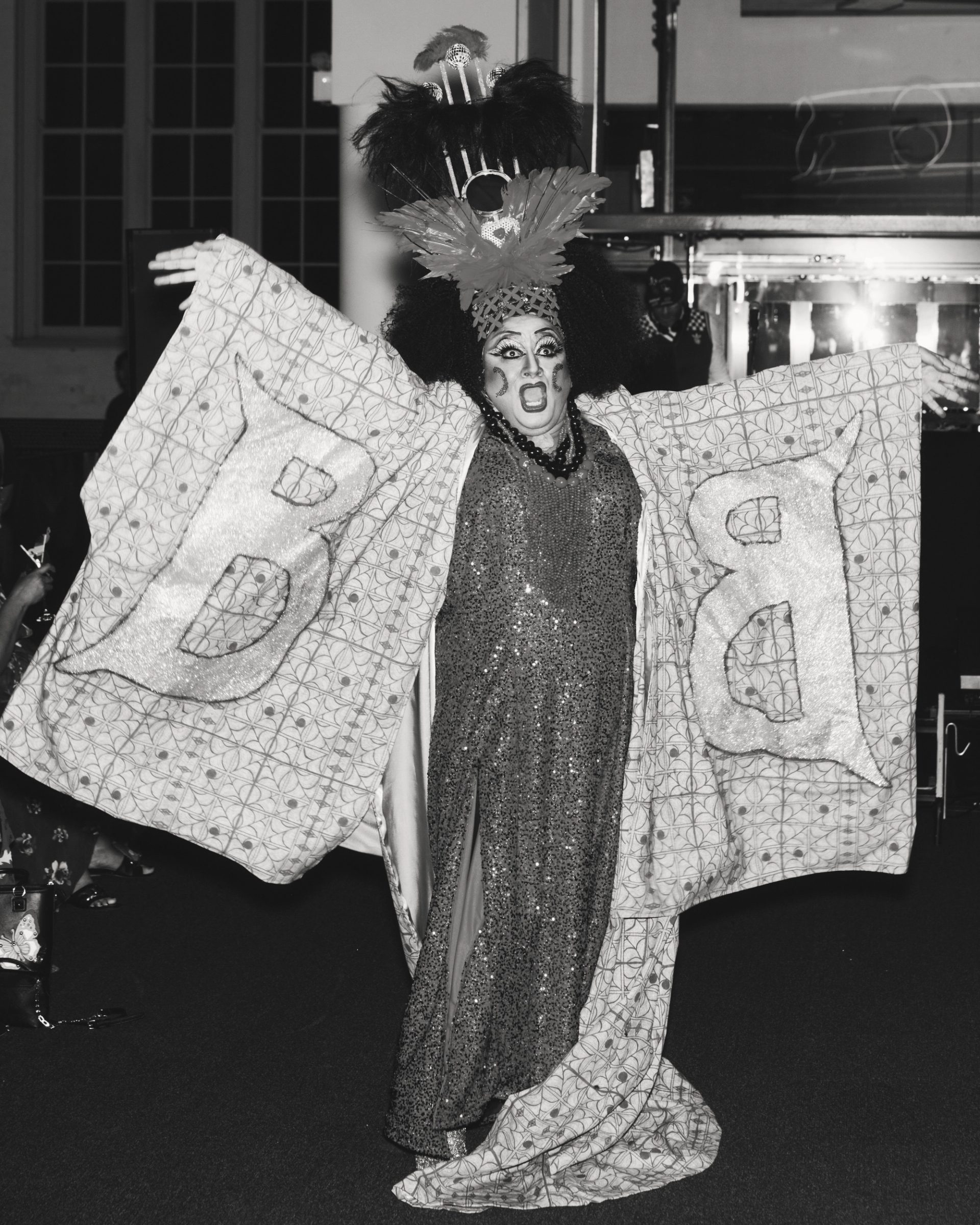 A drag performer performing in a kimono embroidered with large text reading ‘B'