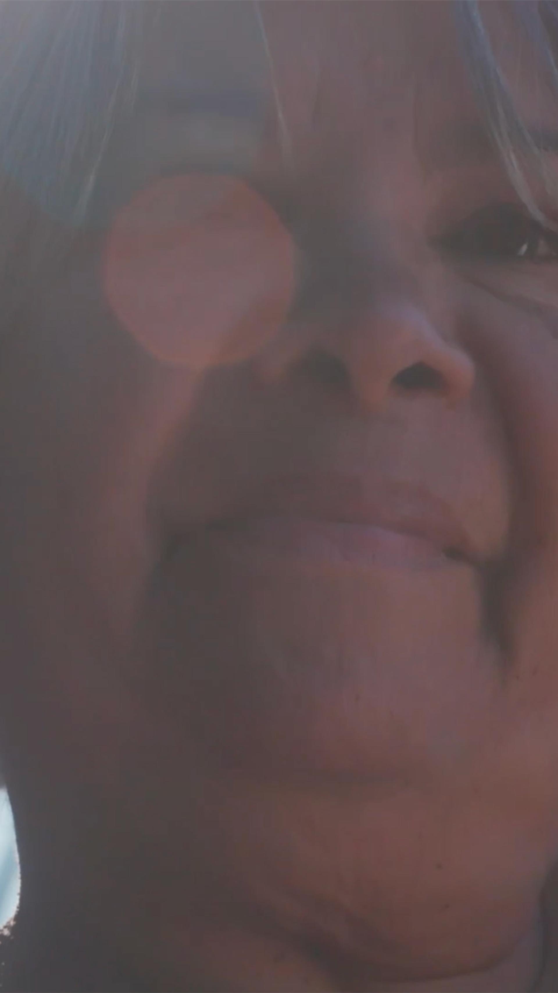A closeup of a woman with white hair in a bob. Her dark eyes look out beyond the camera. Her right eye is obscured by a sunspot.