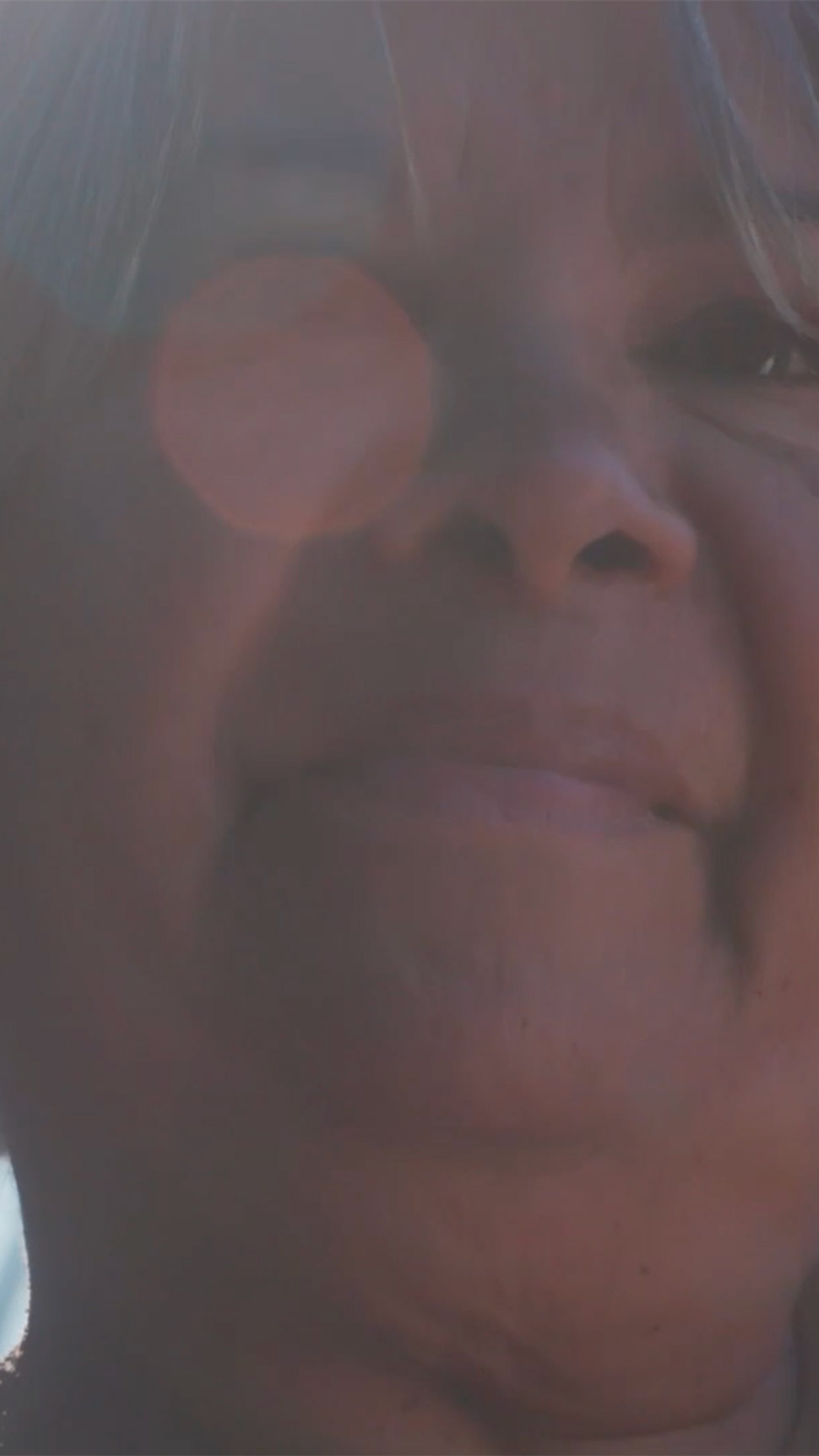 A closeup of a woman with white hair in a bob. Her dark eyes look out beyond the camera. Her right eye is obscured by a sunspot.