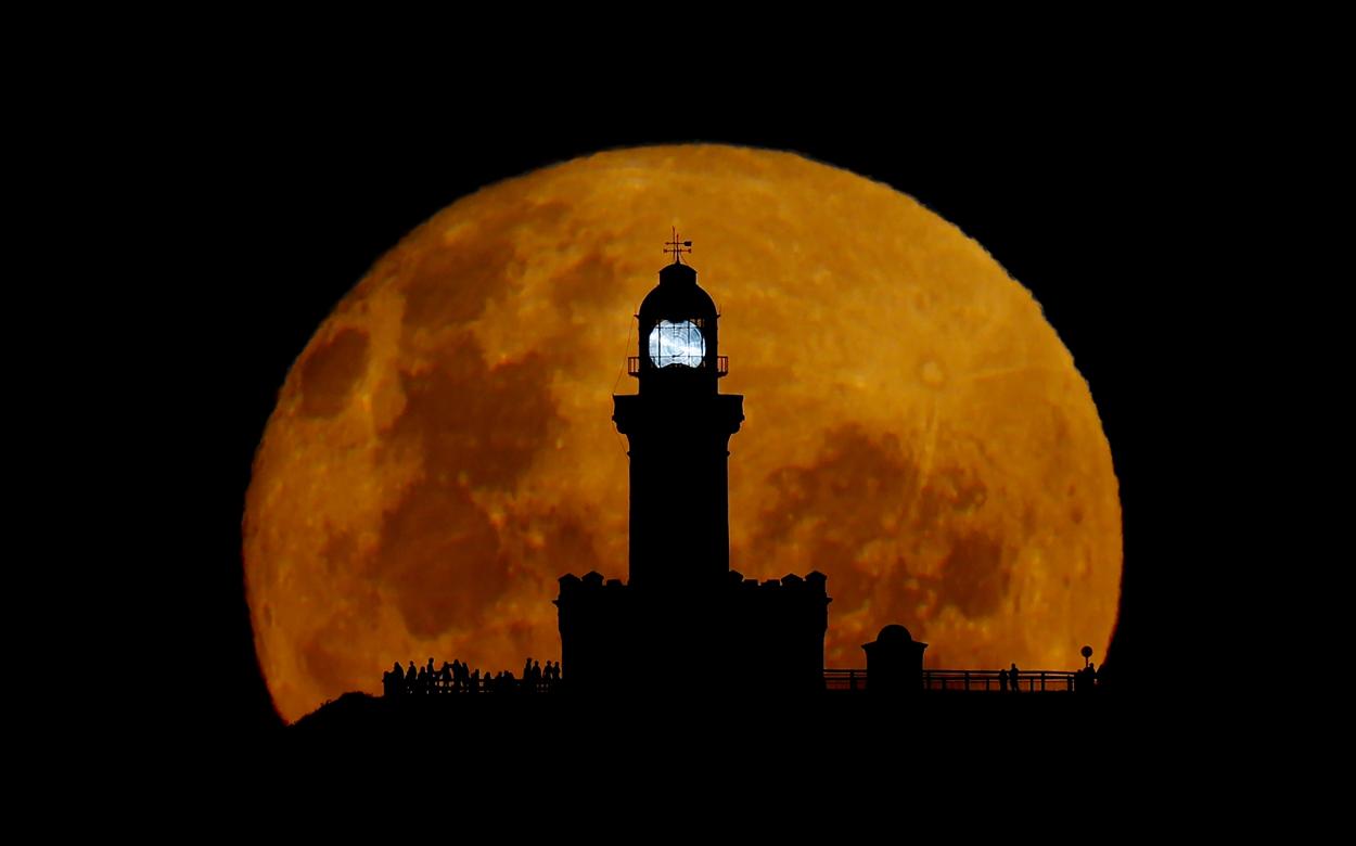 Silhouette of lighthouse in front of a large moon.