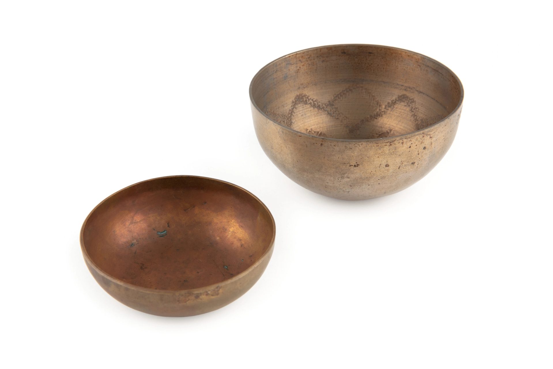 Two bowl-shaped gong parts, made of brass and tombac that have been lathe turned and are hemispherical in shape with a flower petal design in interior.