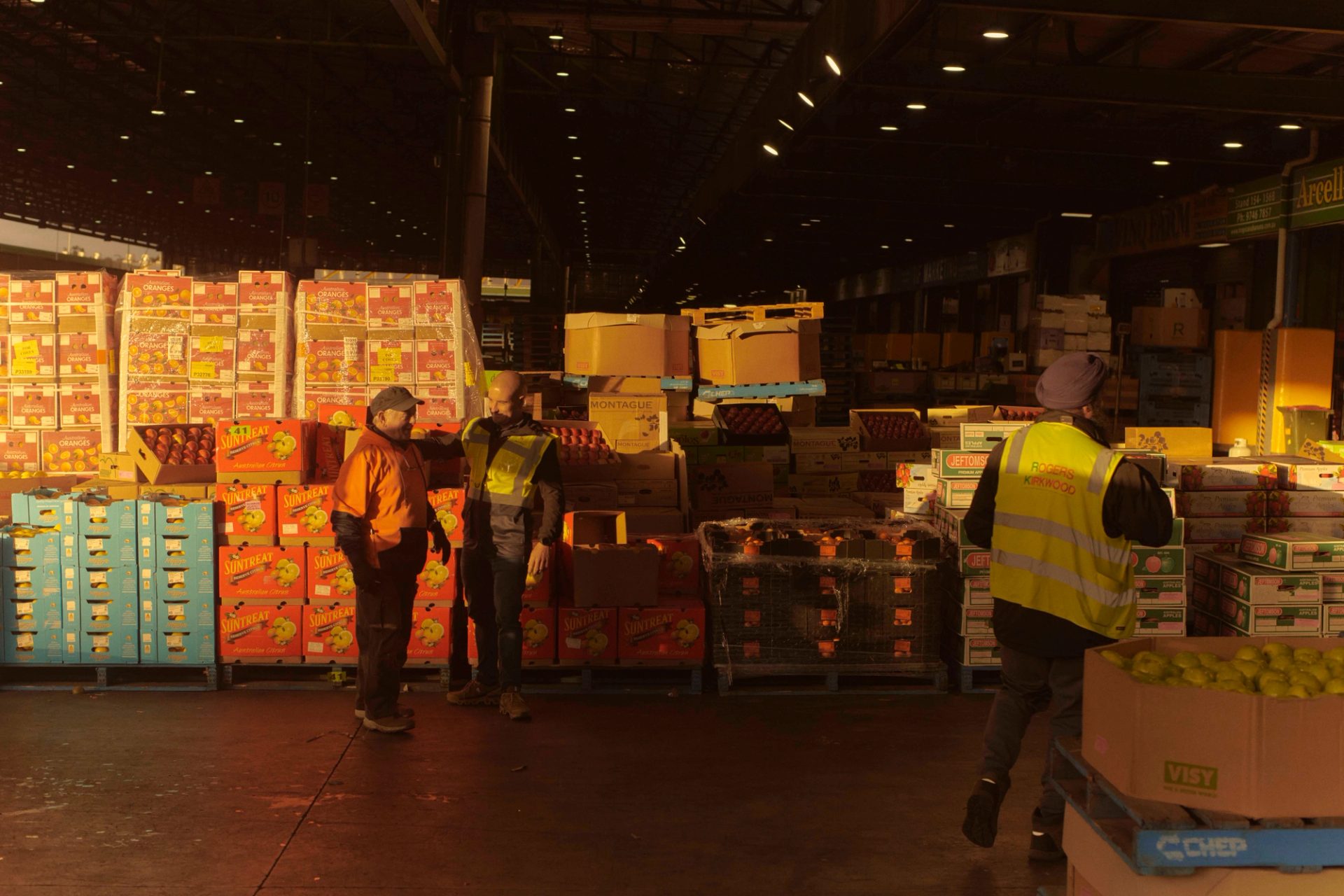 Figures standing in a sunlit market space.