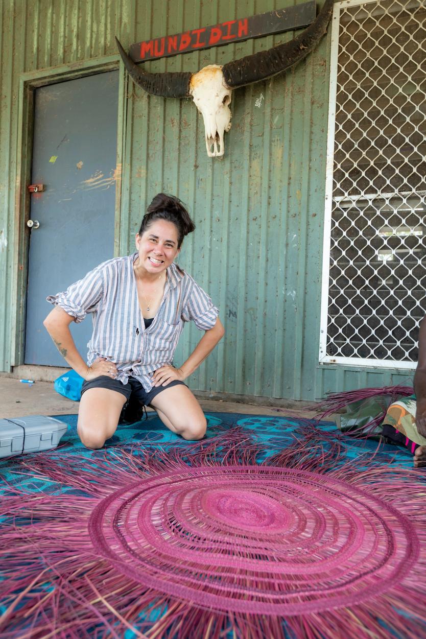 Woman kneeling and smiling over a traditionally woven mat